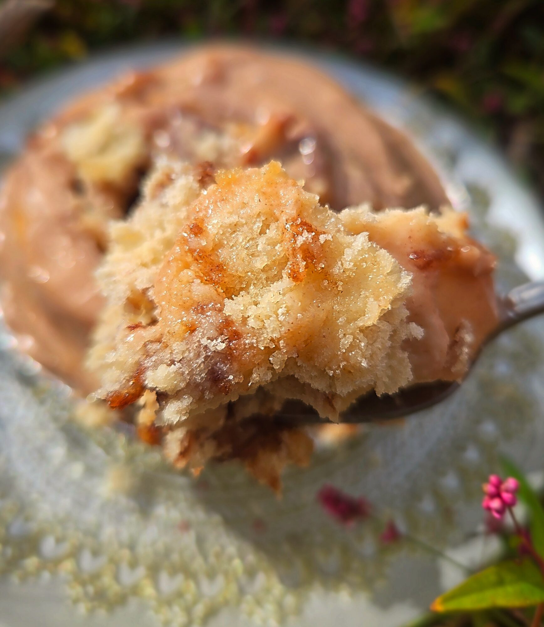 Close-up of a fork holding a piece of cake with frosting, with a blurred cake in the background on a plate.
