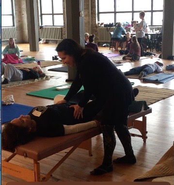 Instructor assisting a person lying on a massage table during a yoga or wellness class in a spacious studio.