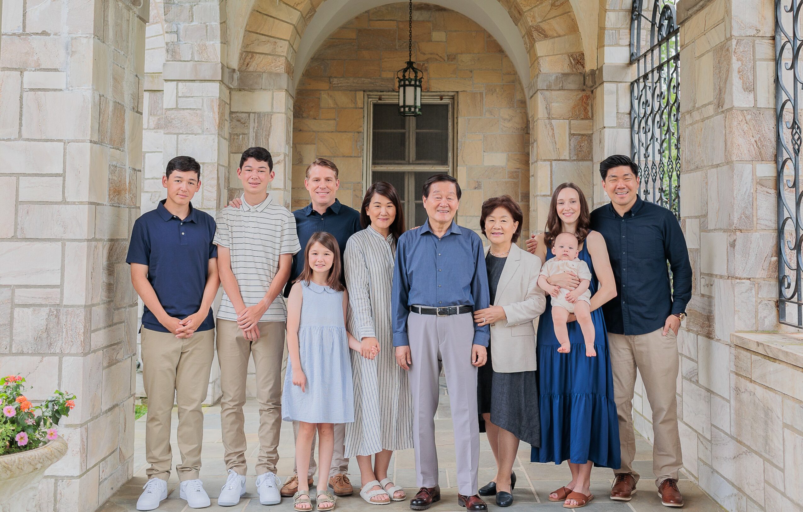 Group of nine people, including children and adults, standing outside a stone building with arches and windows.