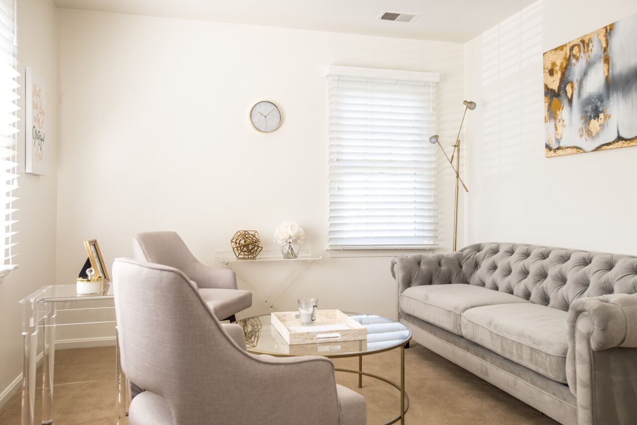 Living room with a gray tufted sofa, two armchairs, a round glass coffee table, and artwork on the wall.