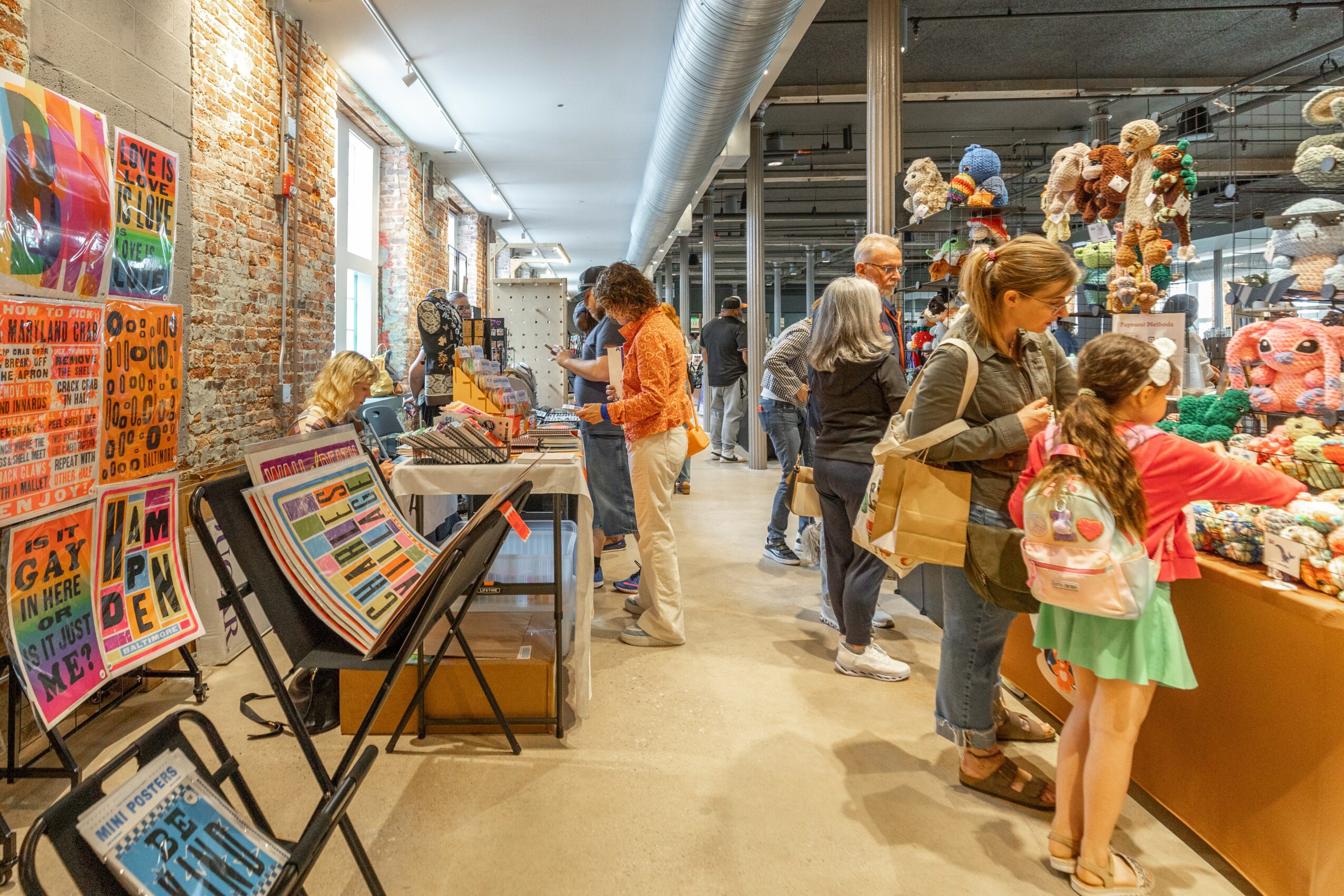 People browsing toys and games in a store with brick walls and large windows, children and adults shopping and exploring items.