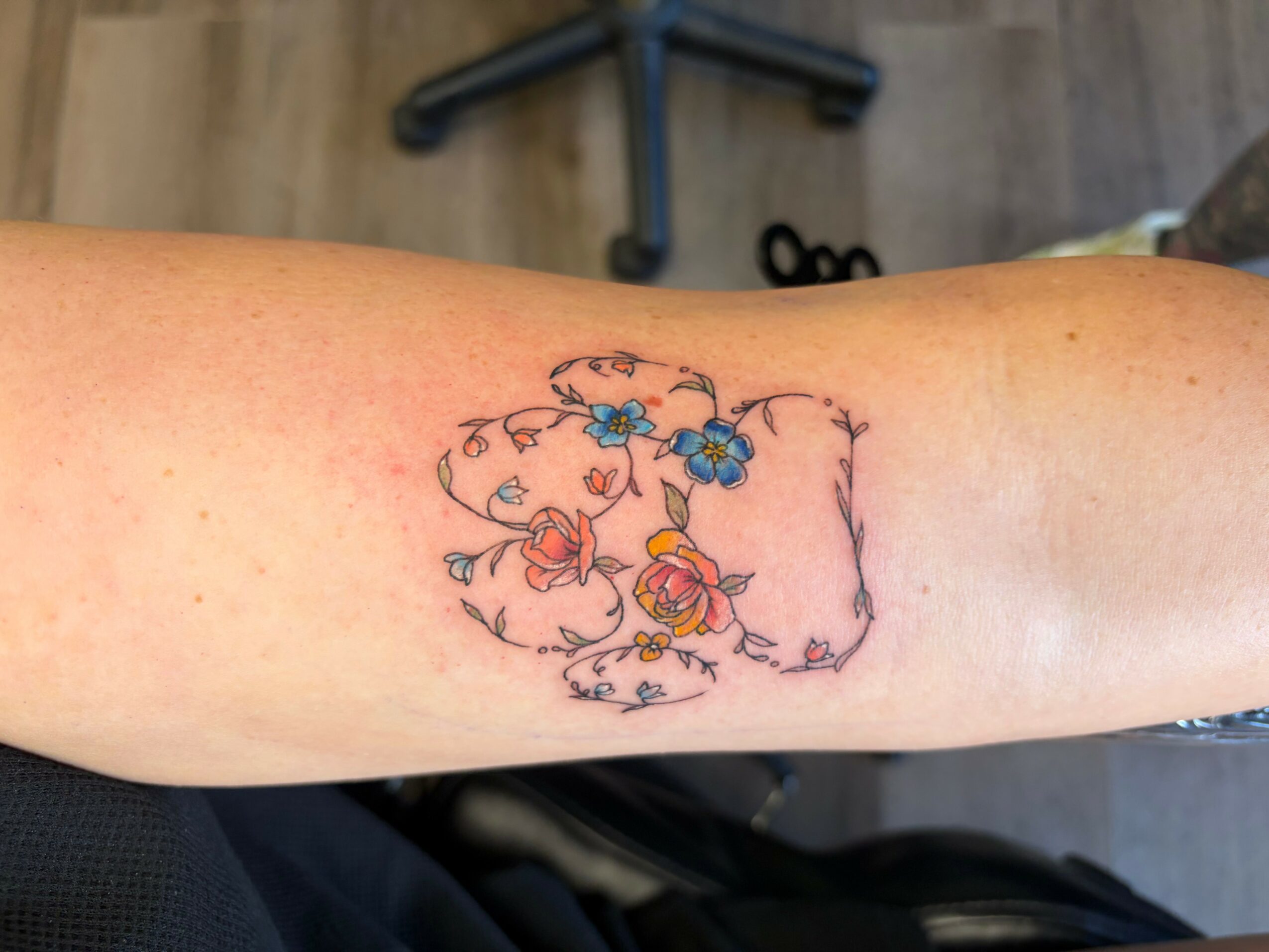 Tattoo of a floral design with colorful flowers and swirling lines on a person's arm.