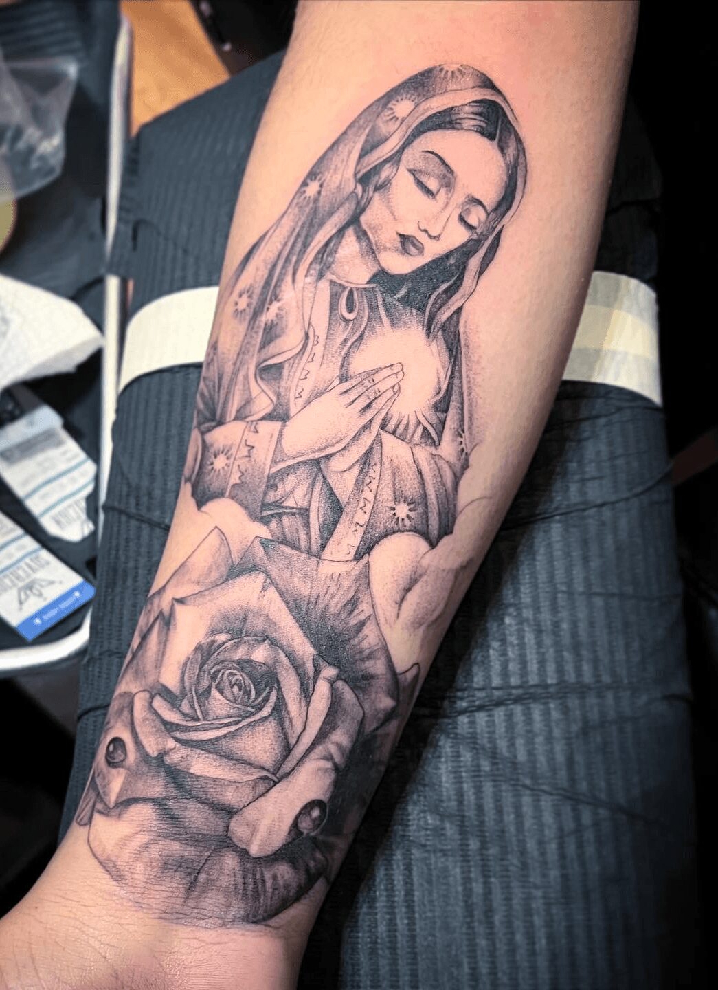 Black and gray tattoo of a woman with hands over her chest, a rose below, and detailed shading.