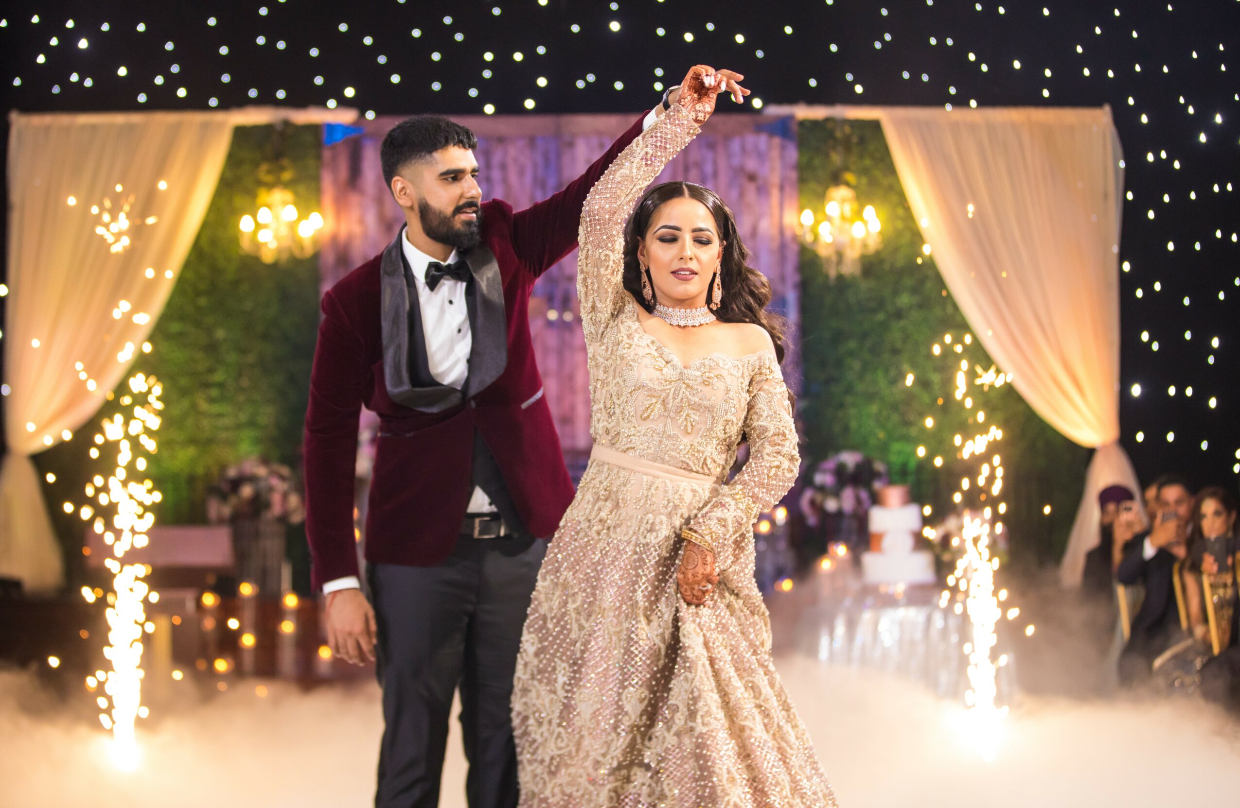A couple dancing at a wedding reception with decorated backdrop and guests in background.