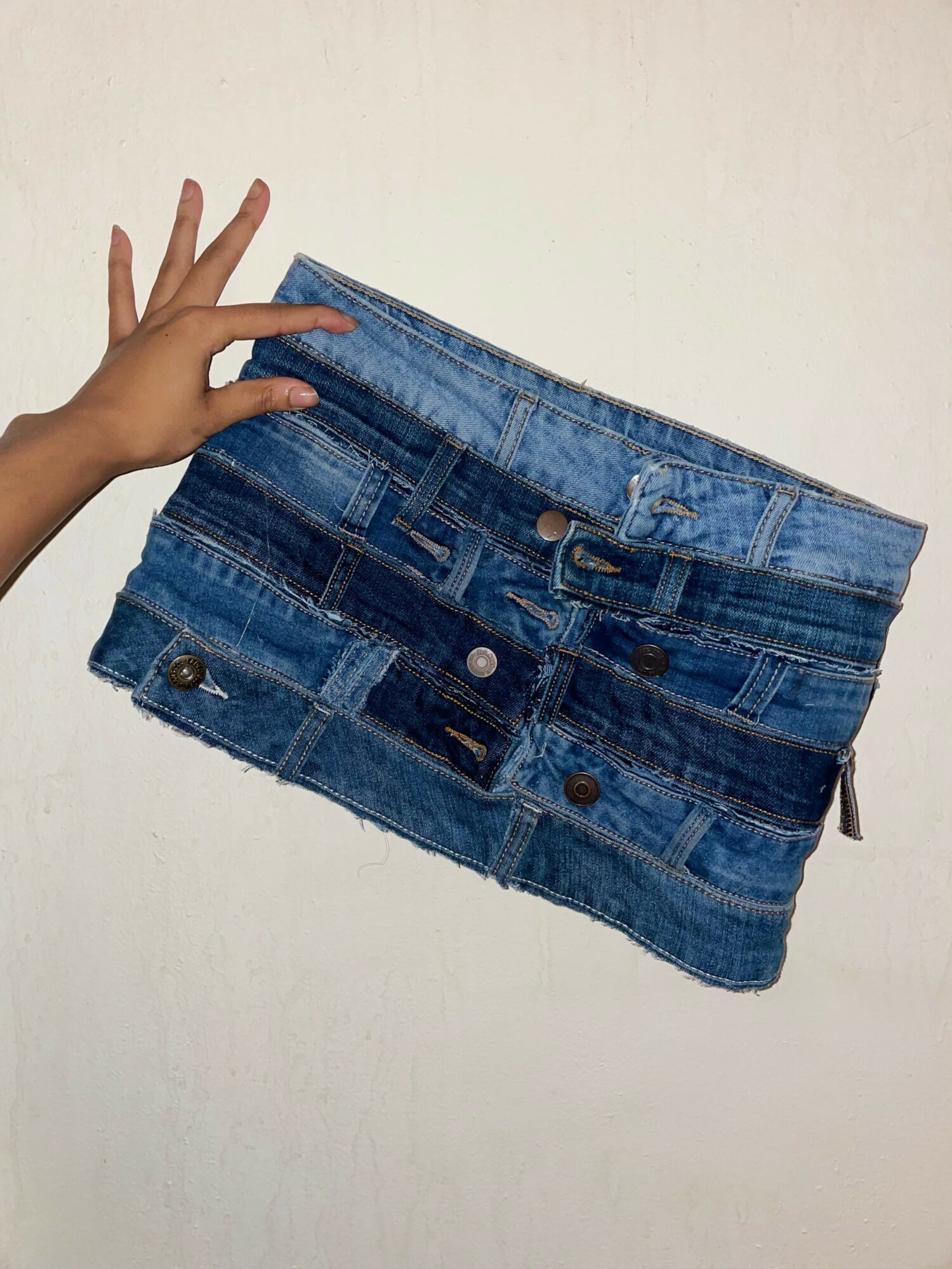Hand holding a stack of folded denim jeans against a plain background.
