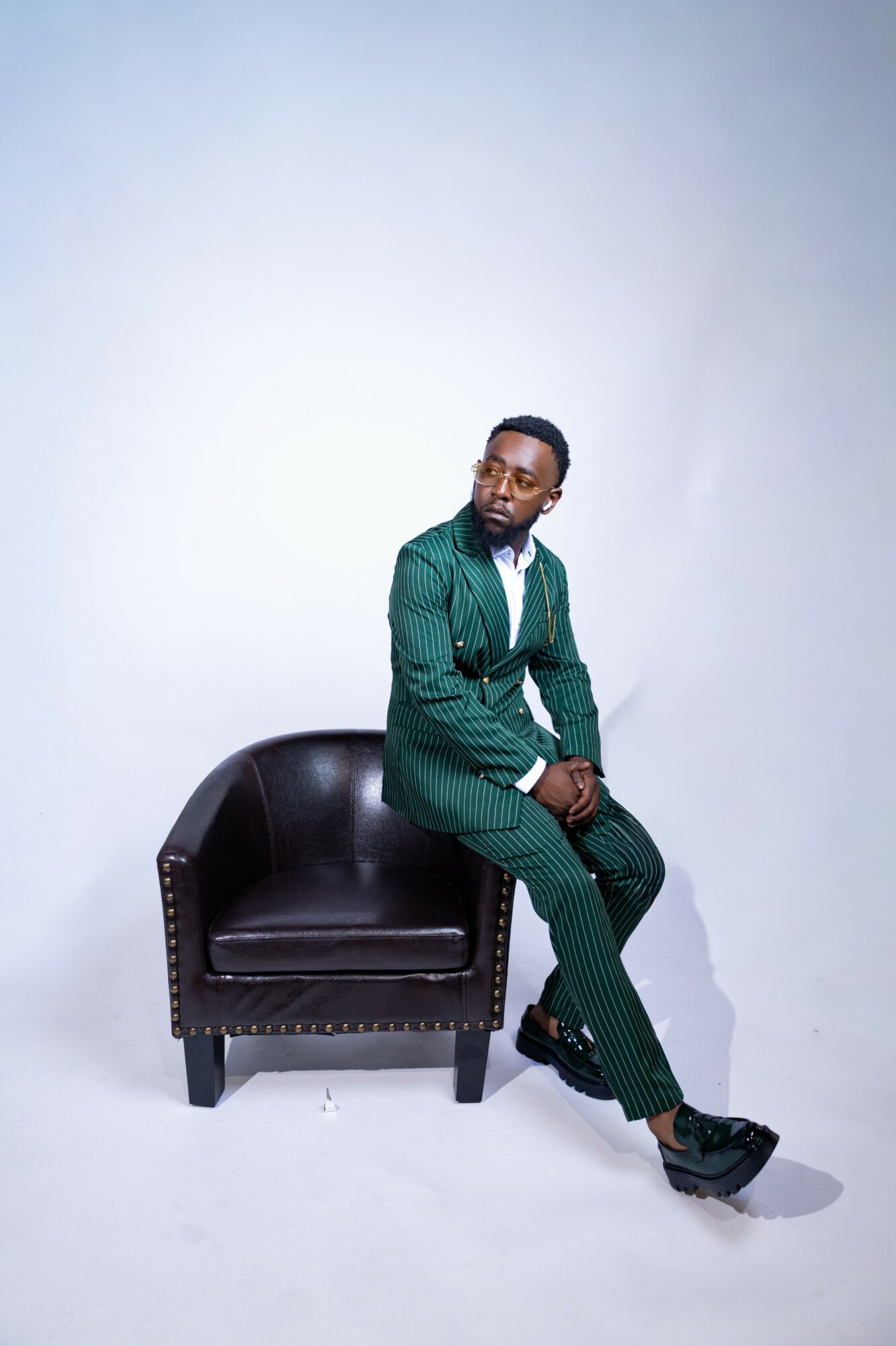 Man in green suit sitting on a black armchair against a plain white background.