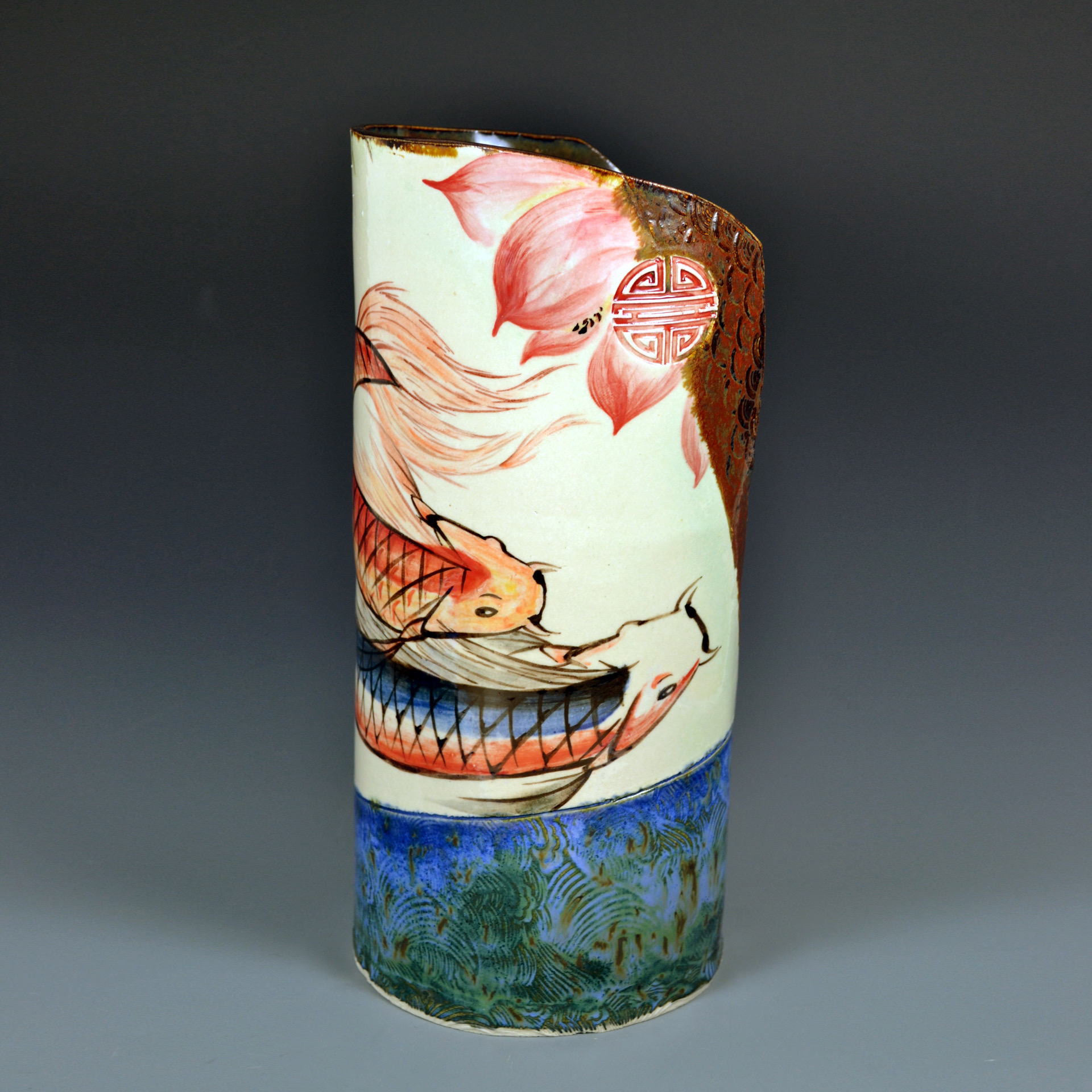 Decorative cylindrical object with painted fish, flowers, and water scene, against a dark background.