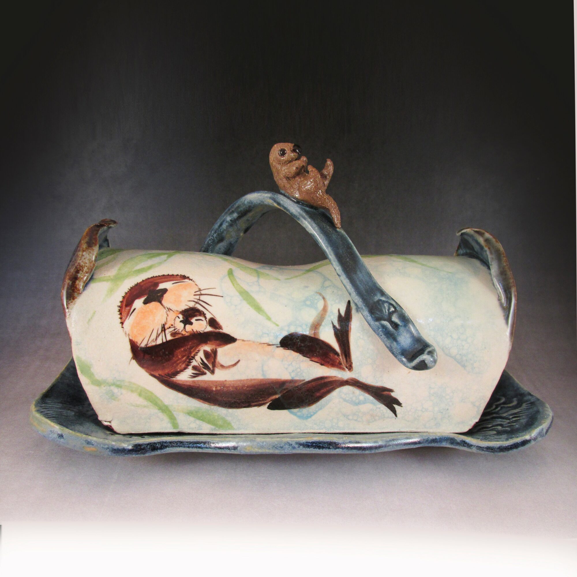 Decorative ceramic dish with fish and a small animal figure, set against a dark background.
