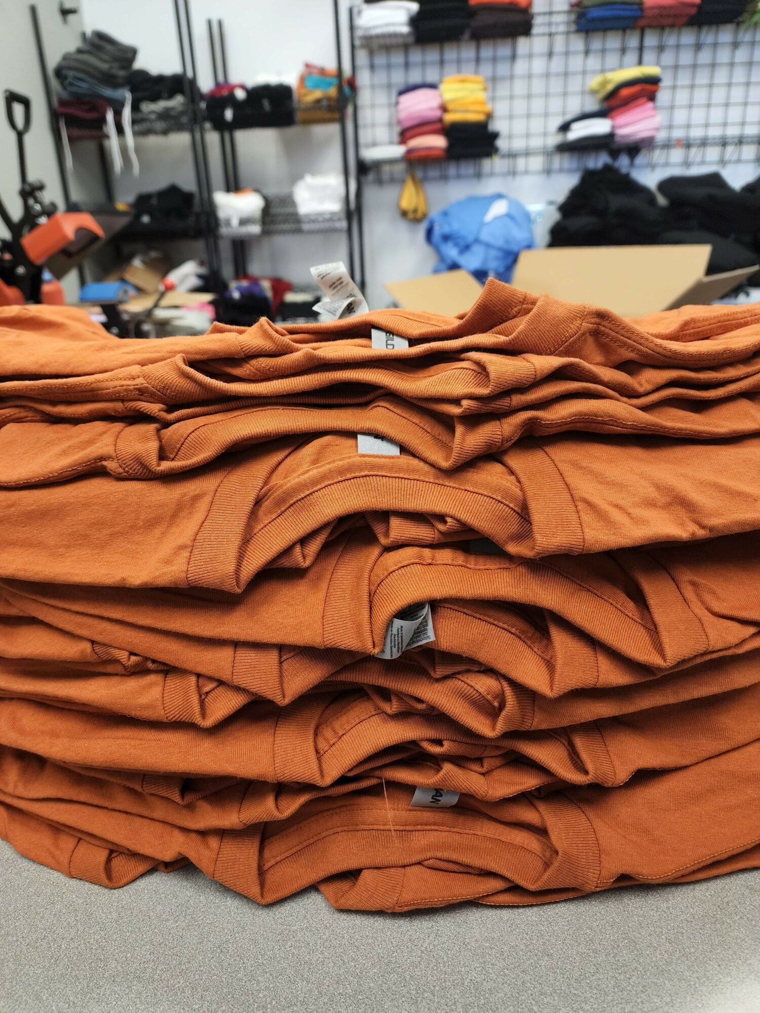 Stack of orange clothing items on a table in a store, with shelves and other products in the background.