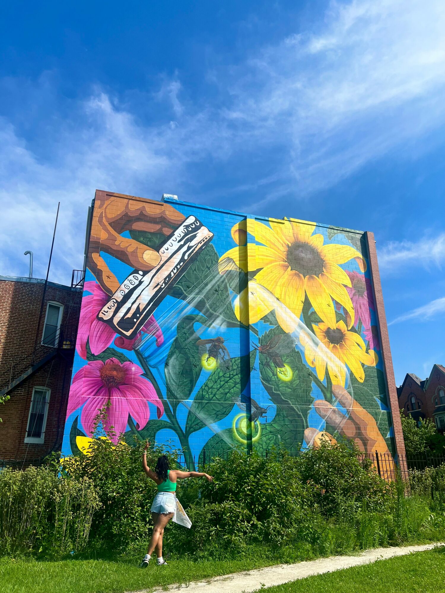 Large colorful mural of flowers and hands on building wall, with a girl running in front, blue sky above.