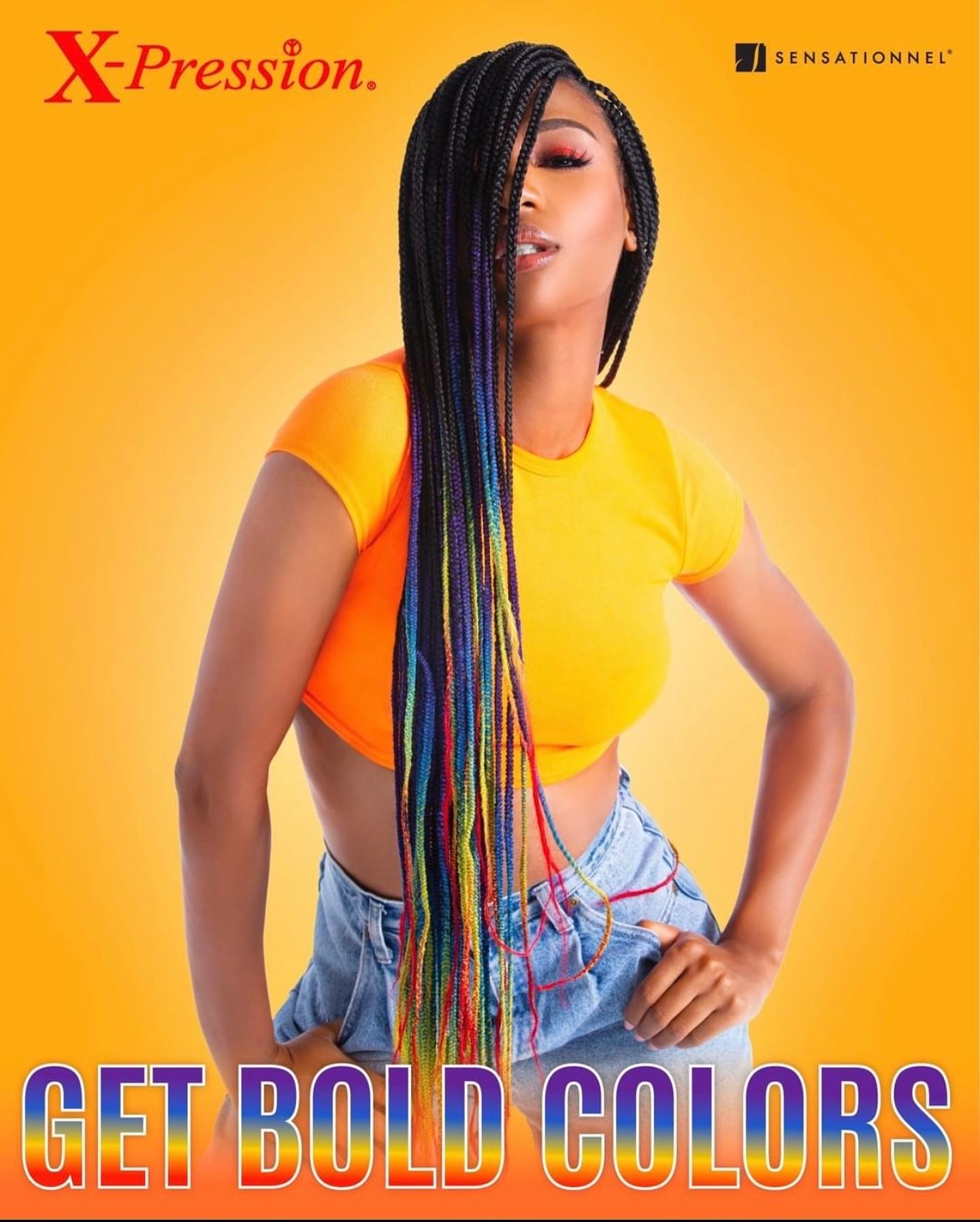 Woman with long, colorful braided hair wearing a yellow crop top and denim shorts, standing against a yellow background.