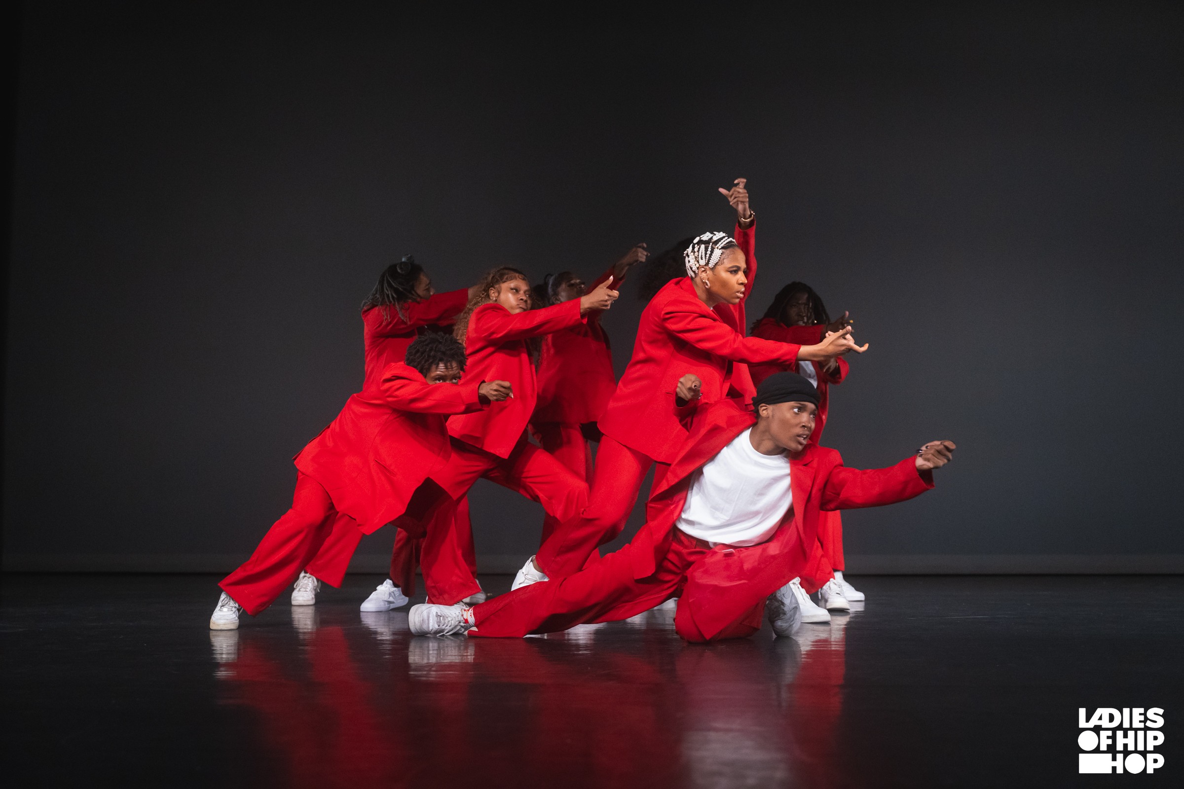 Group of dancers in red and white outfits performing on stage against a dark background.