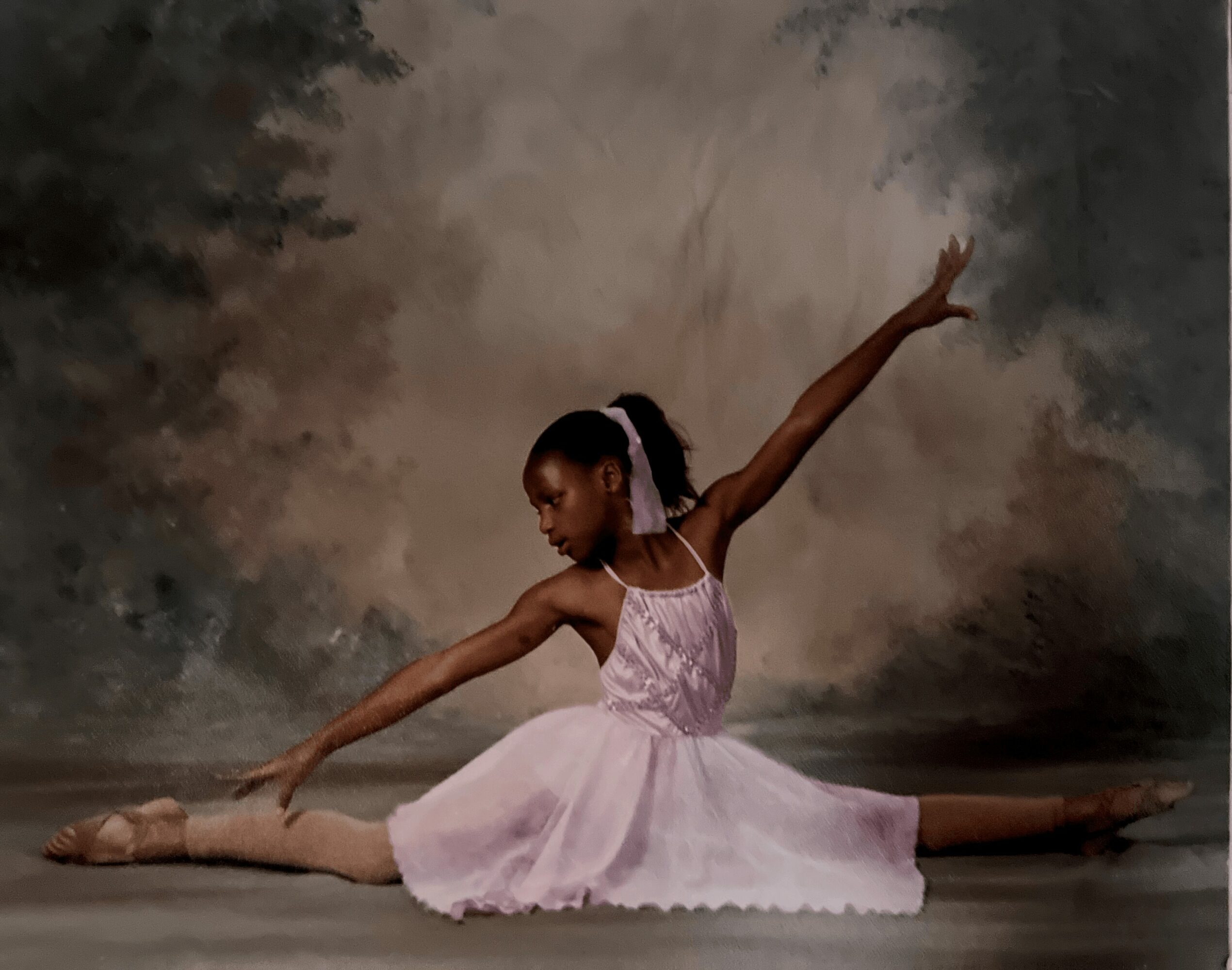 Young girl in pink ballet dress performing a split on stage with a cloudy background.
