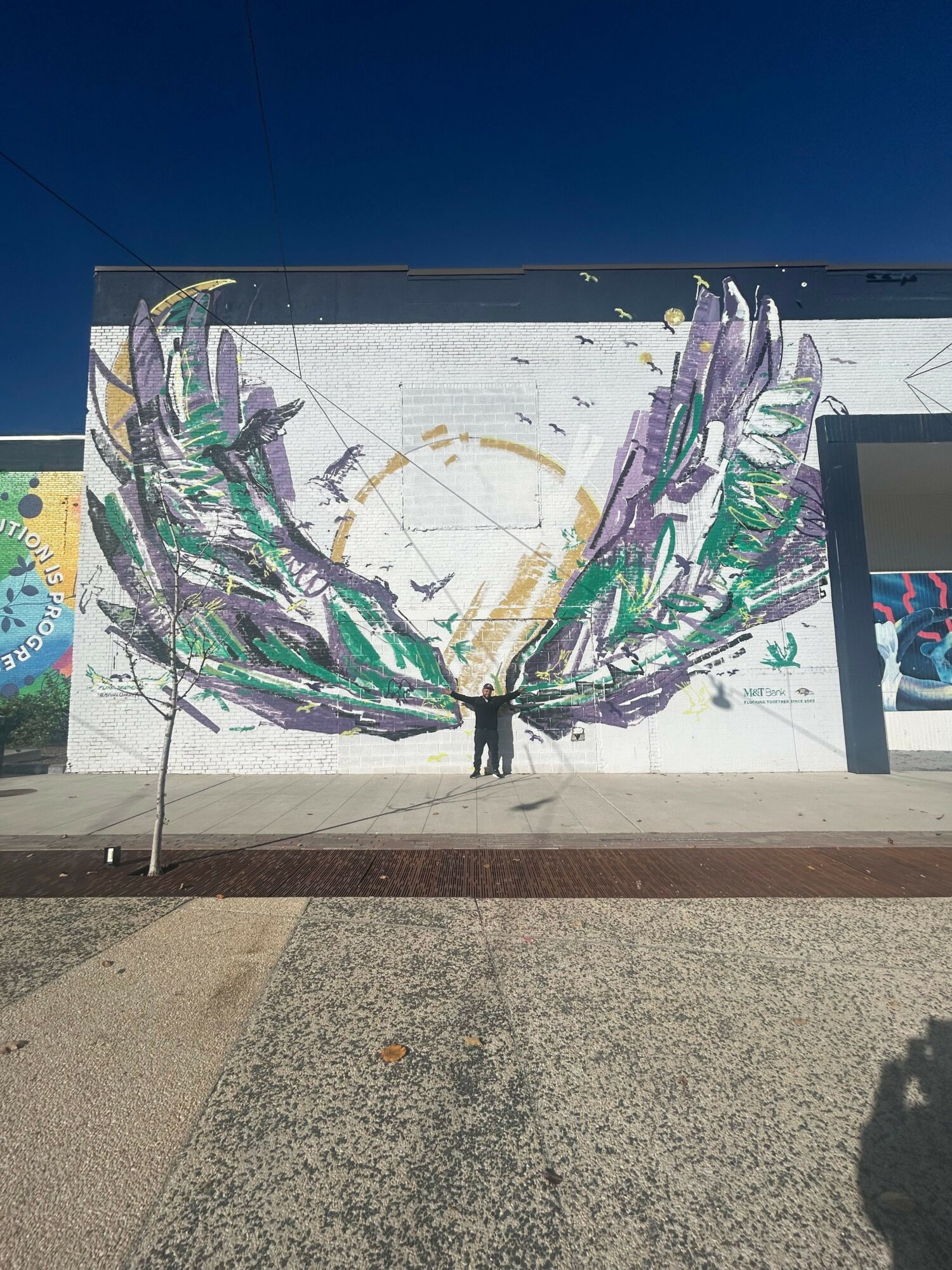 Child's colorful painting of a plant with purple and green leaves on white paper, outdoors on a wall.