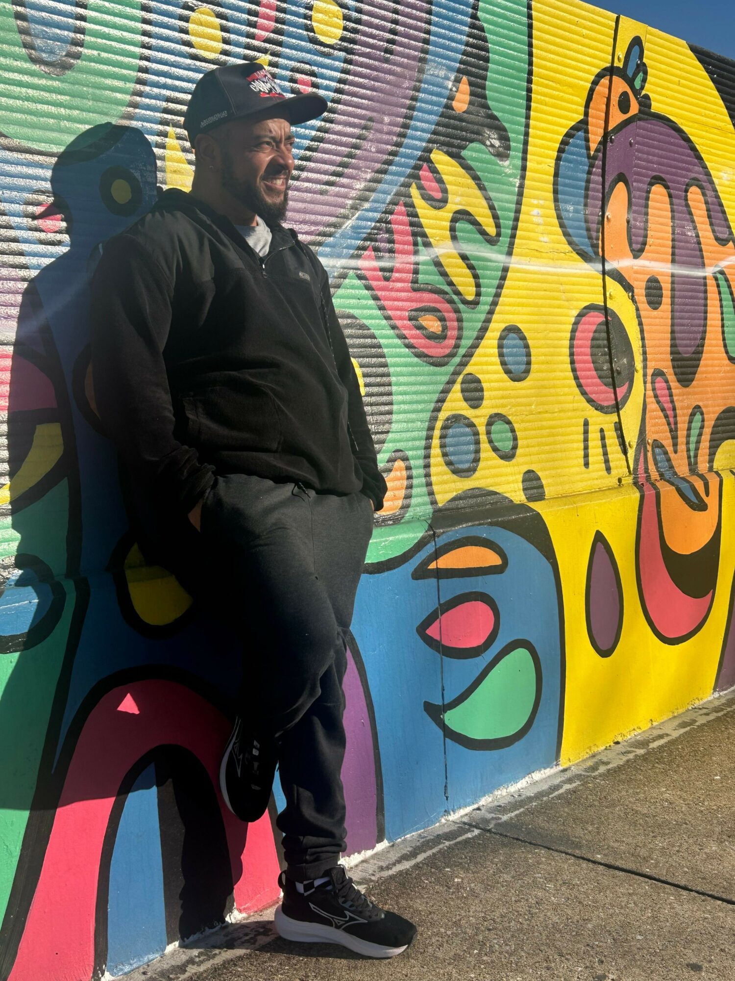 Person lying on colorful, abstract mural with bright shapes and patterns, outdoors on pavement.