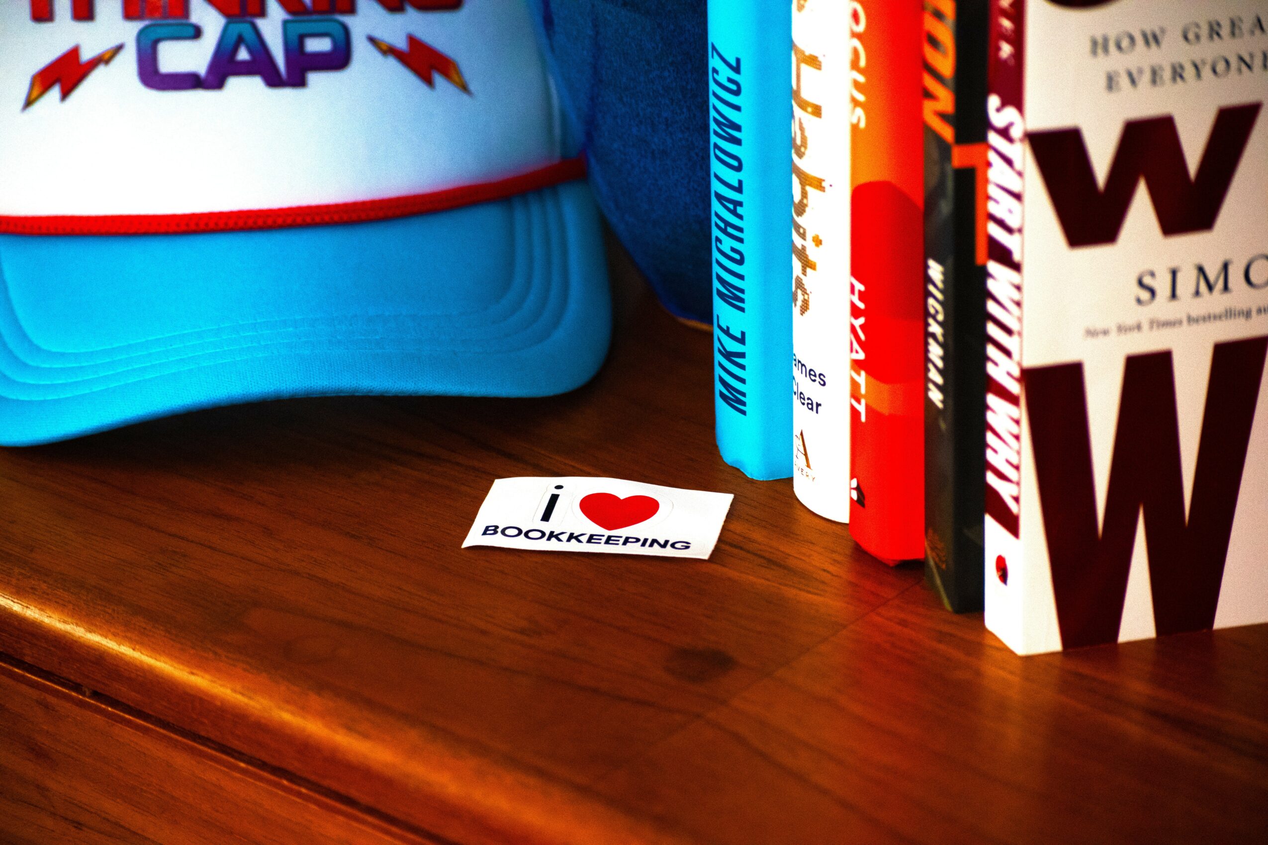 Blue cap with red and white design, books on a wooden surface, and a sticker reading 'I love bookkeeping'.