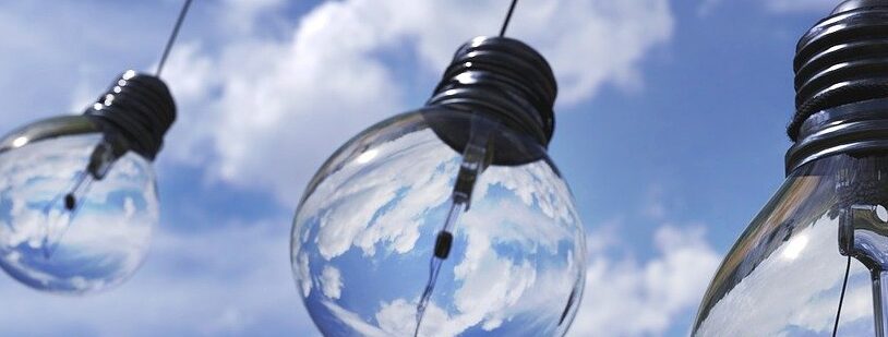 Three hanging light bulbs against a blue sky with clouds, some bulbs are clear and others are frosted.