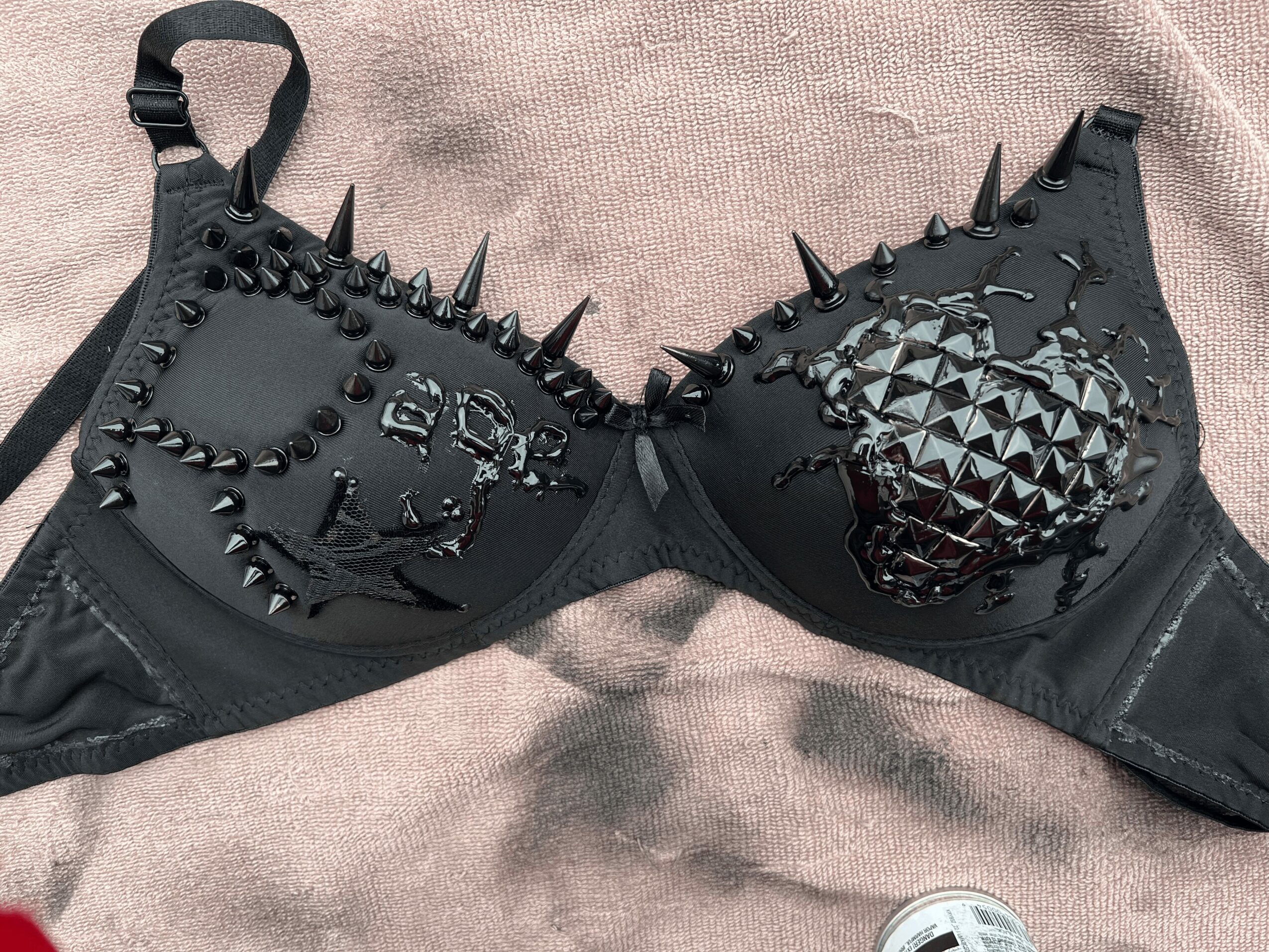 Black bra with spikes and metallic skull designs on the cups, lying on a fabric surface.