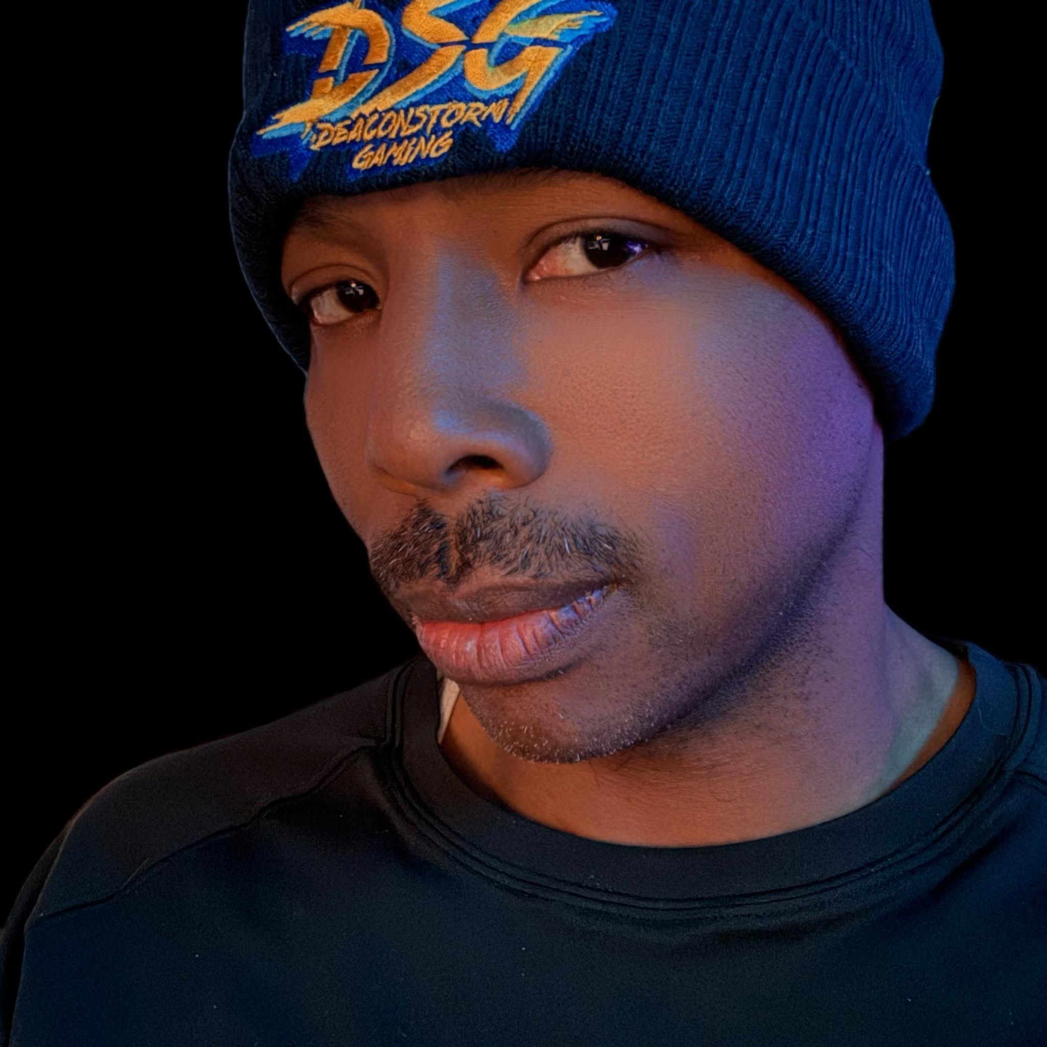 Close-up of a person wearing a blue beanie with colorful logo, looking at the camera, with a dark background.