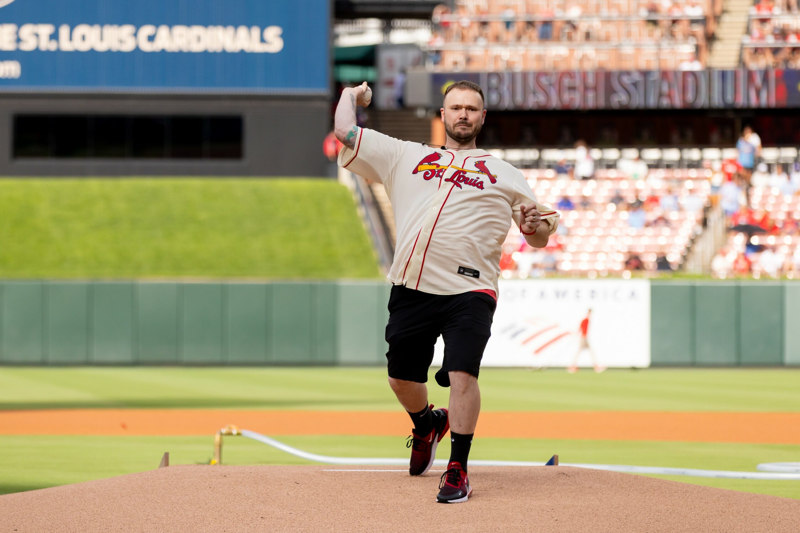 Man in baseball uniform on field, holding a baseball glove, with stadium seats in background.
