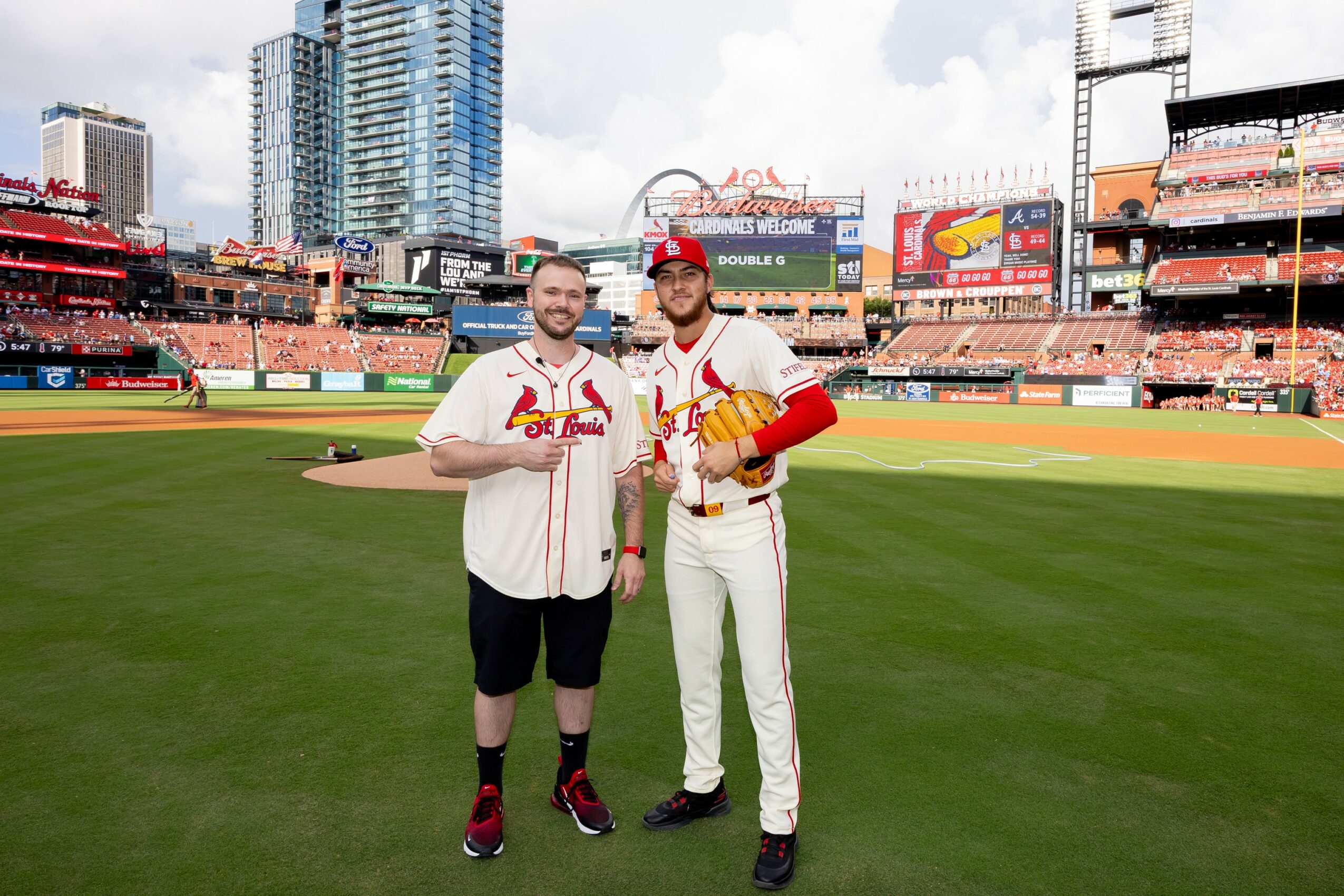 Two baseball players in uniform standing on a field with a stadium and city skyline in the background.