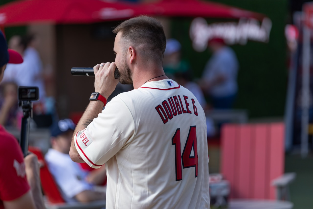 Person in a white sports jersey with number 14 and name Double G, holding a microphone, at a sports event