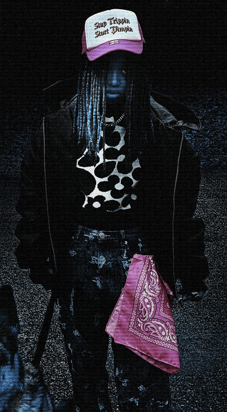 Person wearing a pink and white cap, black jacket, polka dot shirt, and pink bandana, standing in darkness.