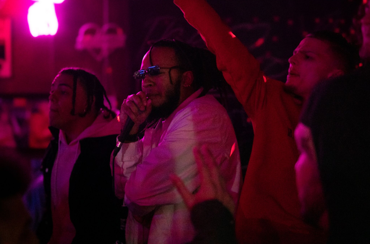 People dancing and enjoying music in a dimly lit club with pink and purple lighting.