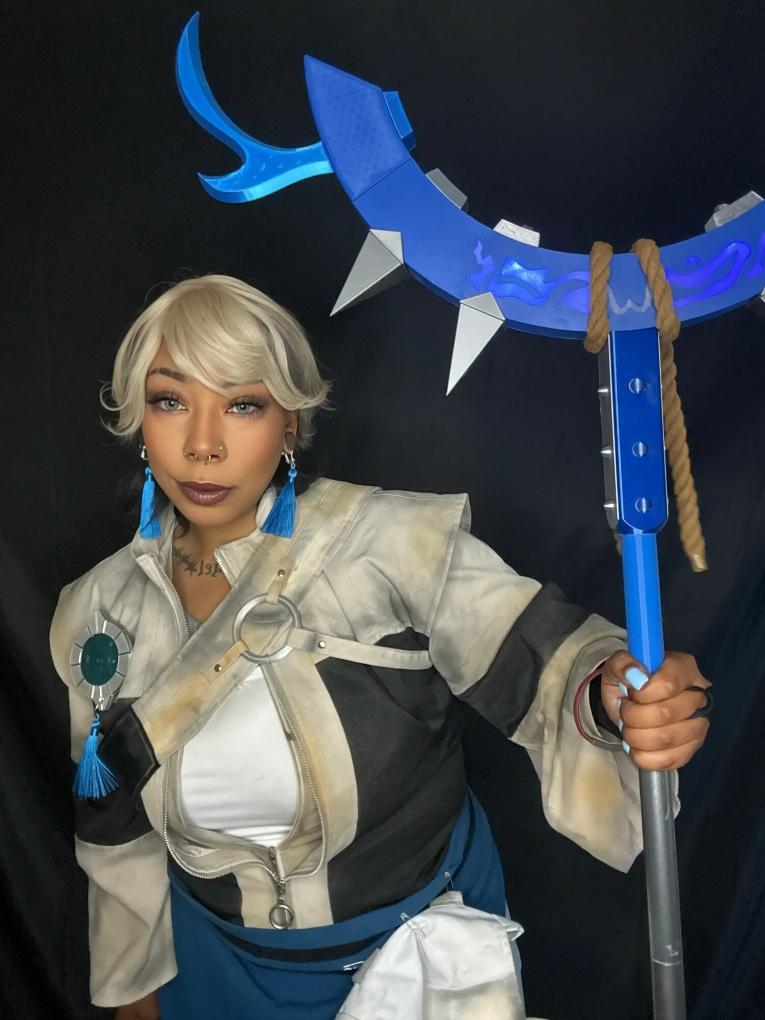 Person in costume holding a large blue and gray weapon with spikes, wearing a white and gray outfit with blue accessories.
