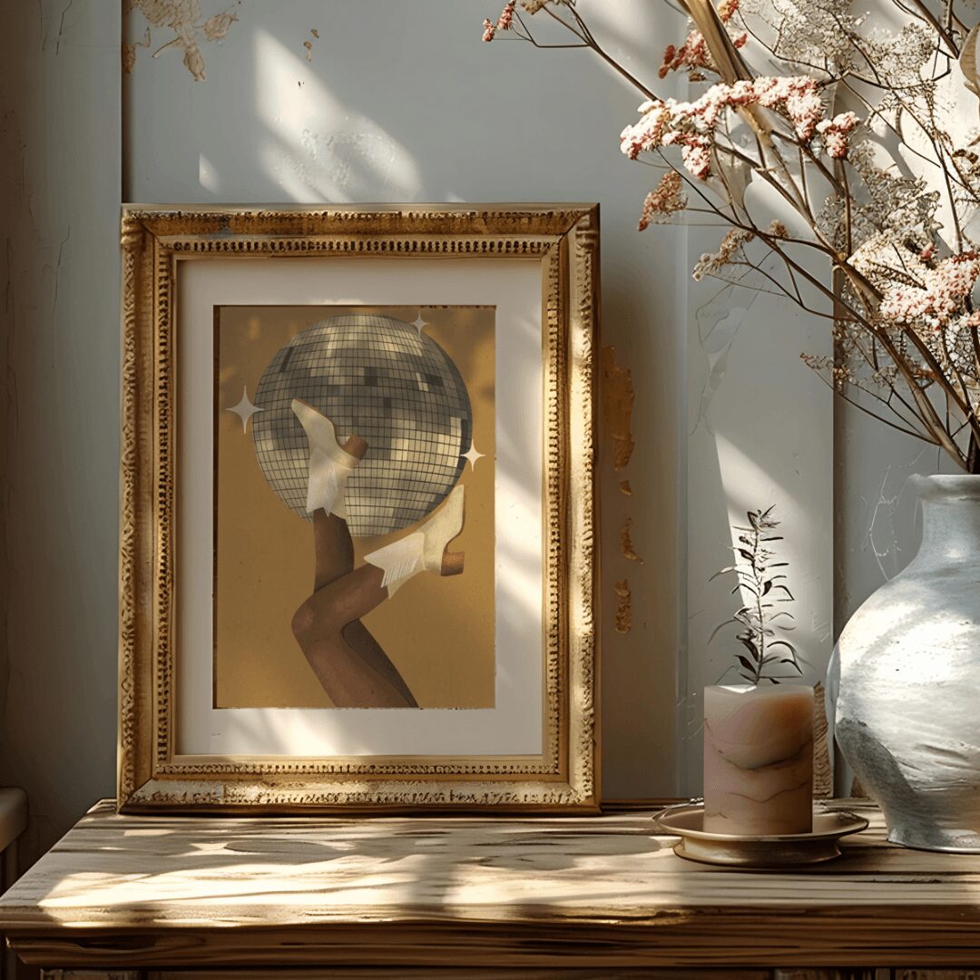 Framed artwork of a person holding a disco ball, with a vase of pink flowers and a candle on a wooden surface.