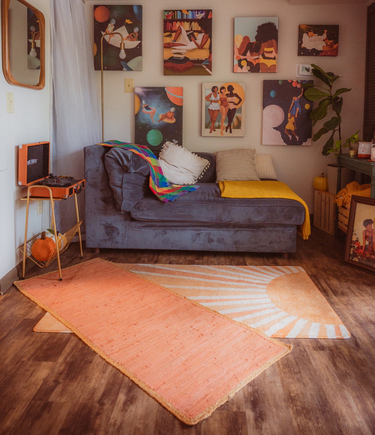 Living room with a gray sofa, colorful artwork on the wall, a small side table, and two rugs on wooden floor.