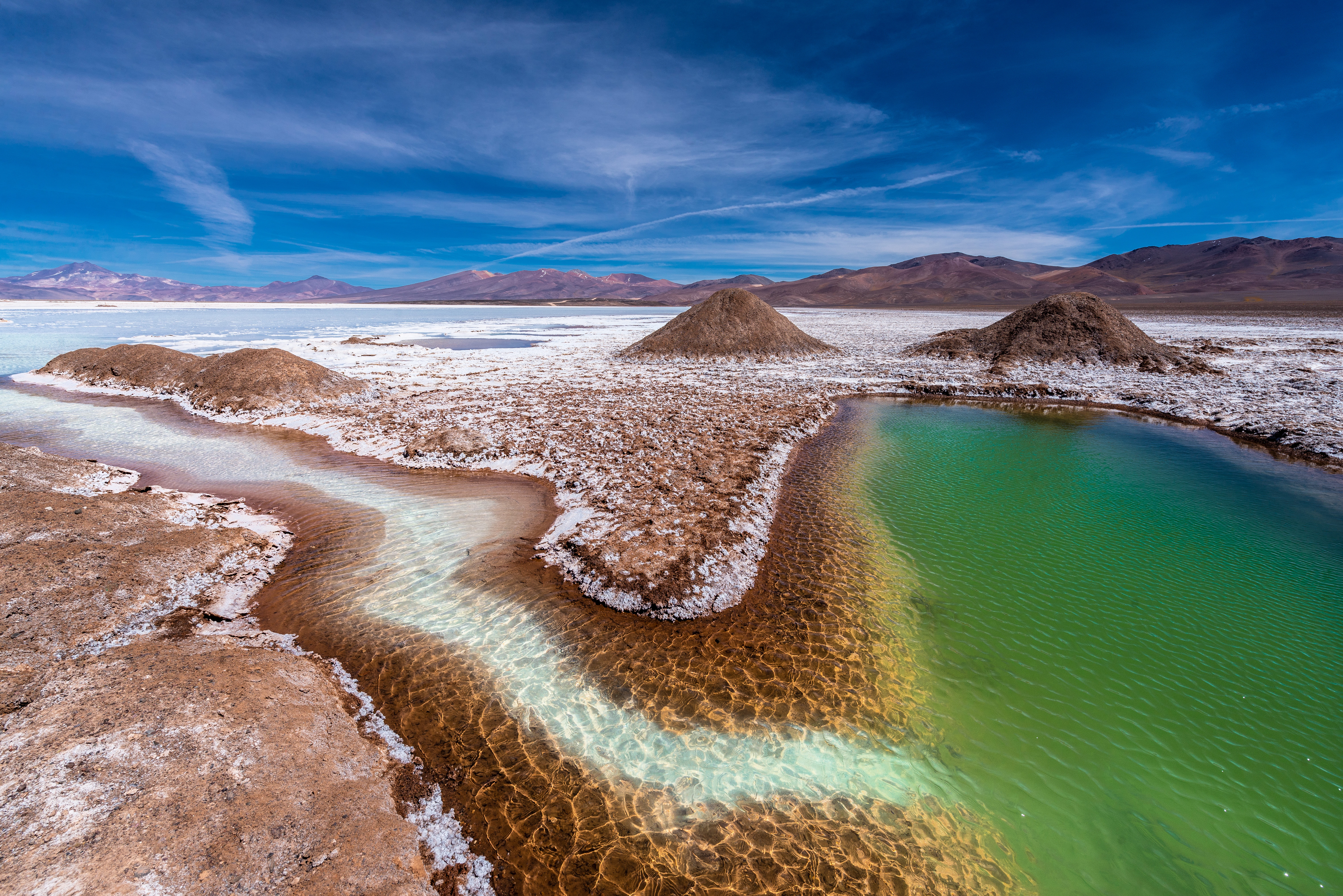 Landscape with colorful lakes, hills, and a blue sky with clouds, in a desert area.