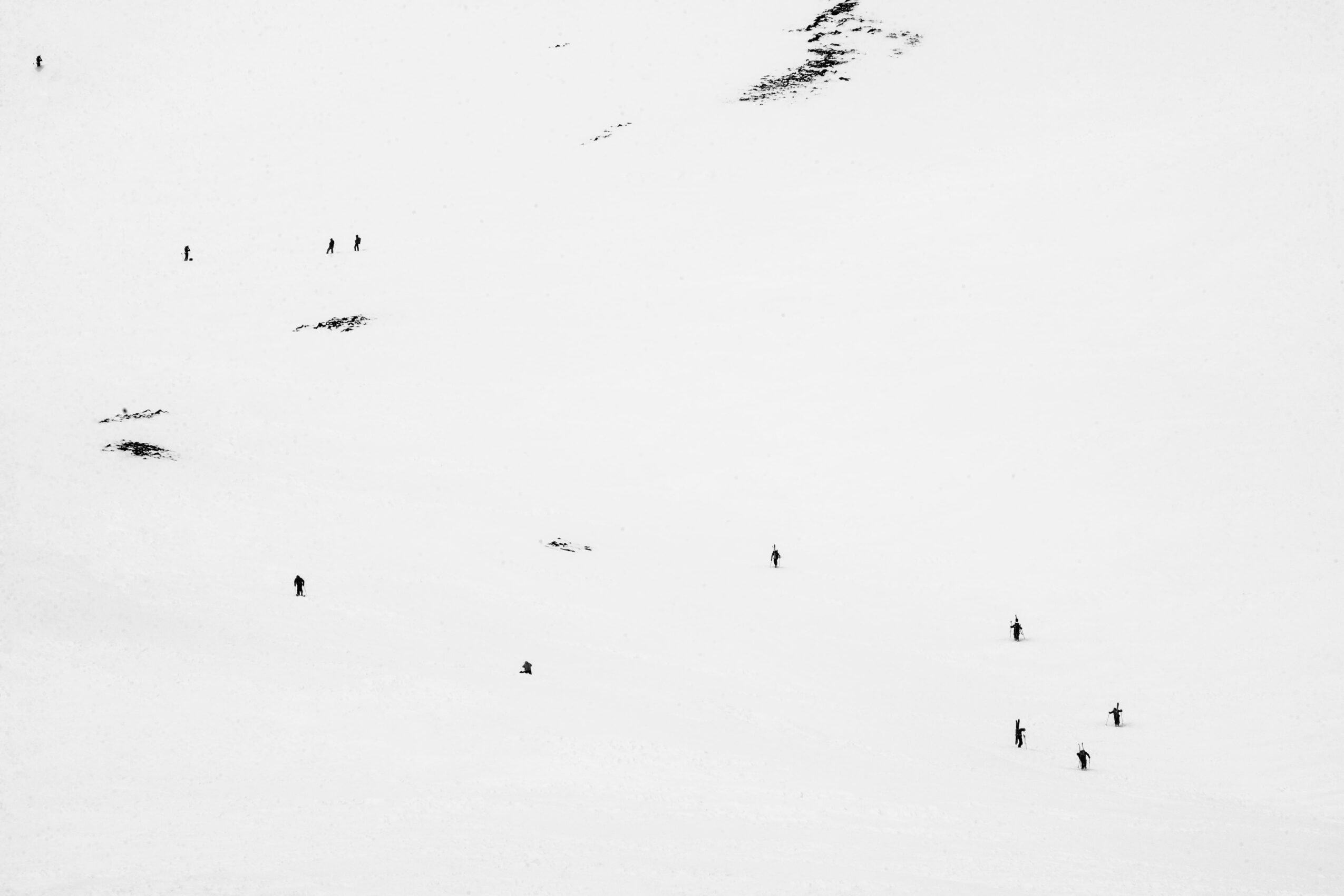 Snow-covered landscape with small dark figures scattered across the snow, some near the top and others near the bottom.
