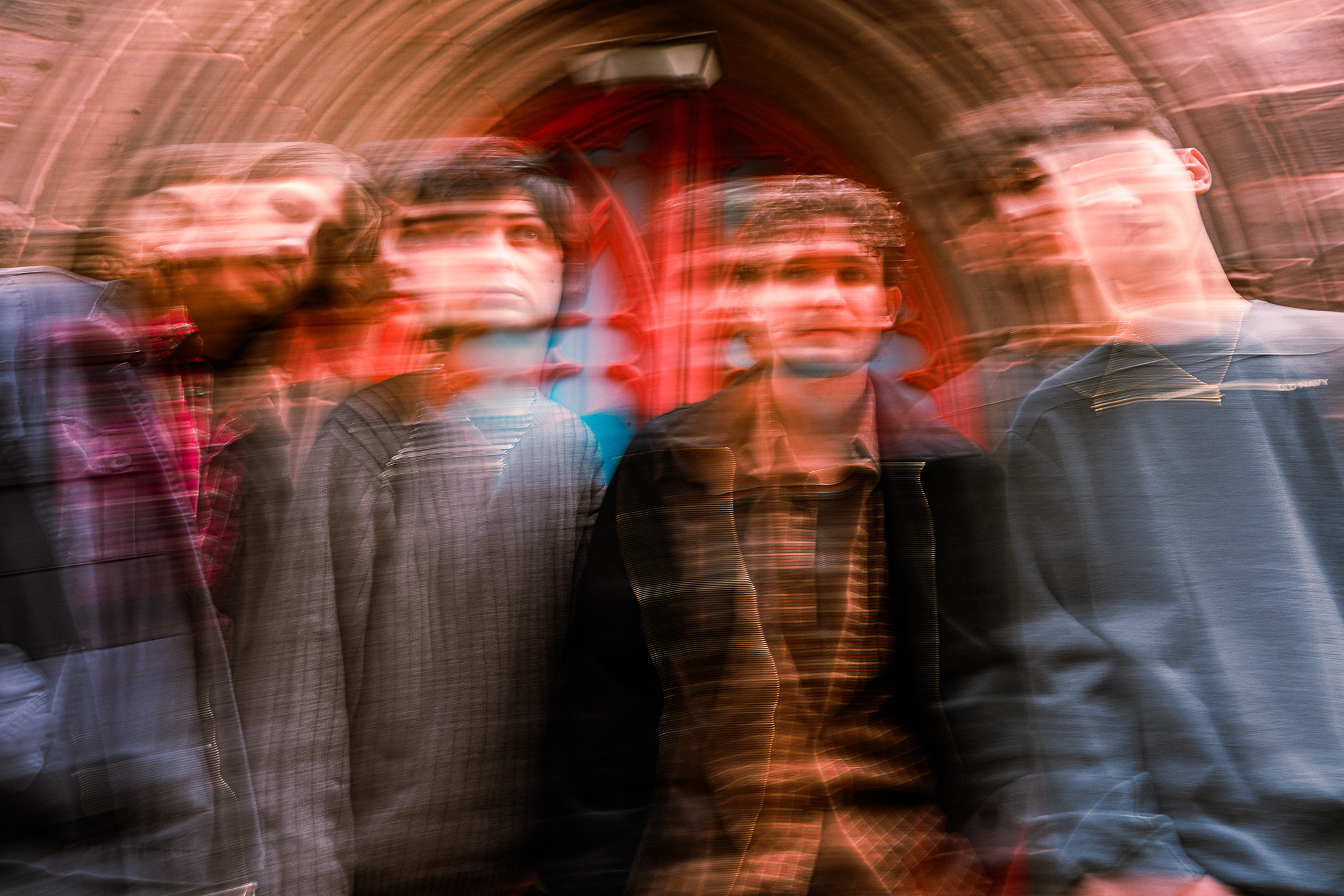 Blurred group of five people standing indoors with a red door in the background.