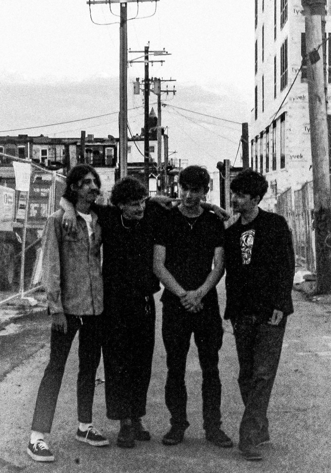 Four people standing on a street with buildings and utility poles in the background.