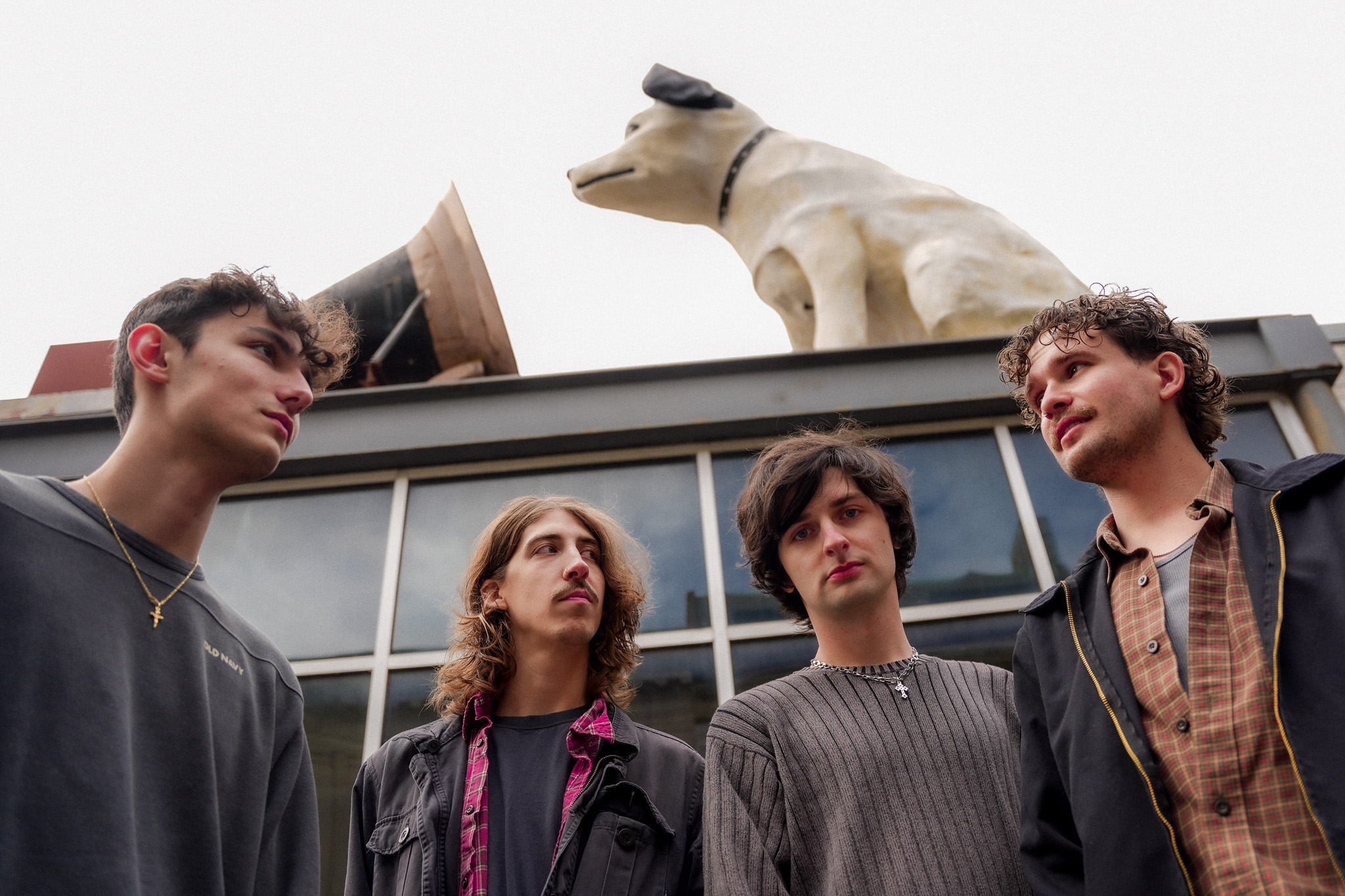 Four people stand in front of a building with a large animal statue on the roof, looking up at it.