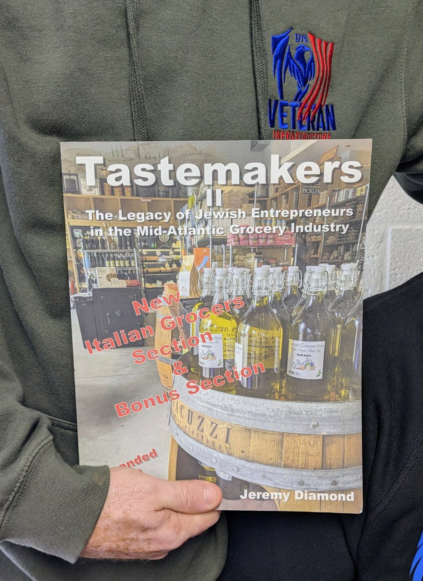 Person holding a magazine titled 'Tastemakers' with bottles on a barrel on the cover, and a logo on clothing. Word count: 20
