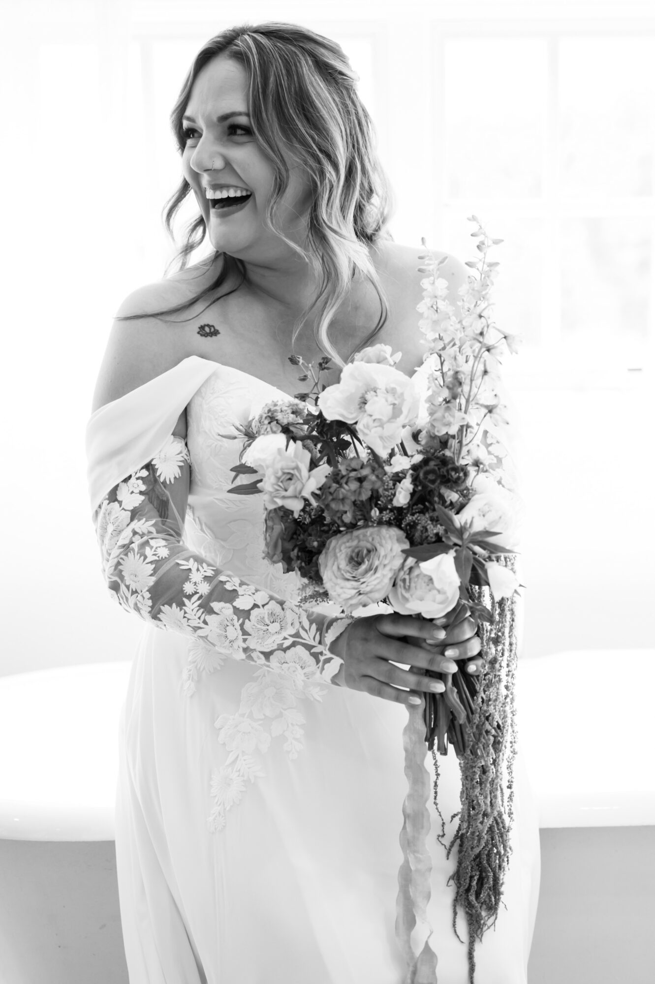 Woman in wedding dress holding a bouquet, smiling, with long wavy hair, in a bright room.