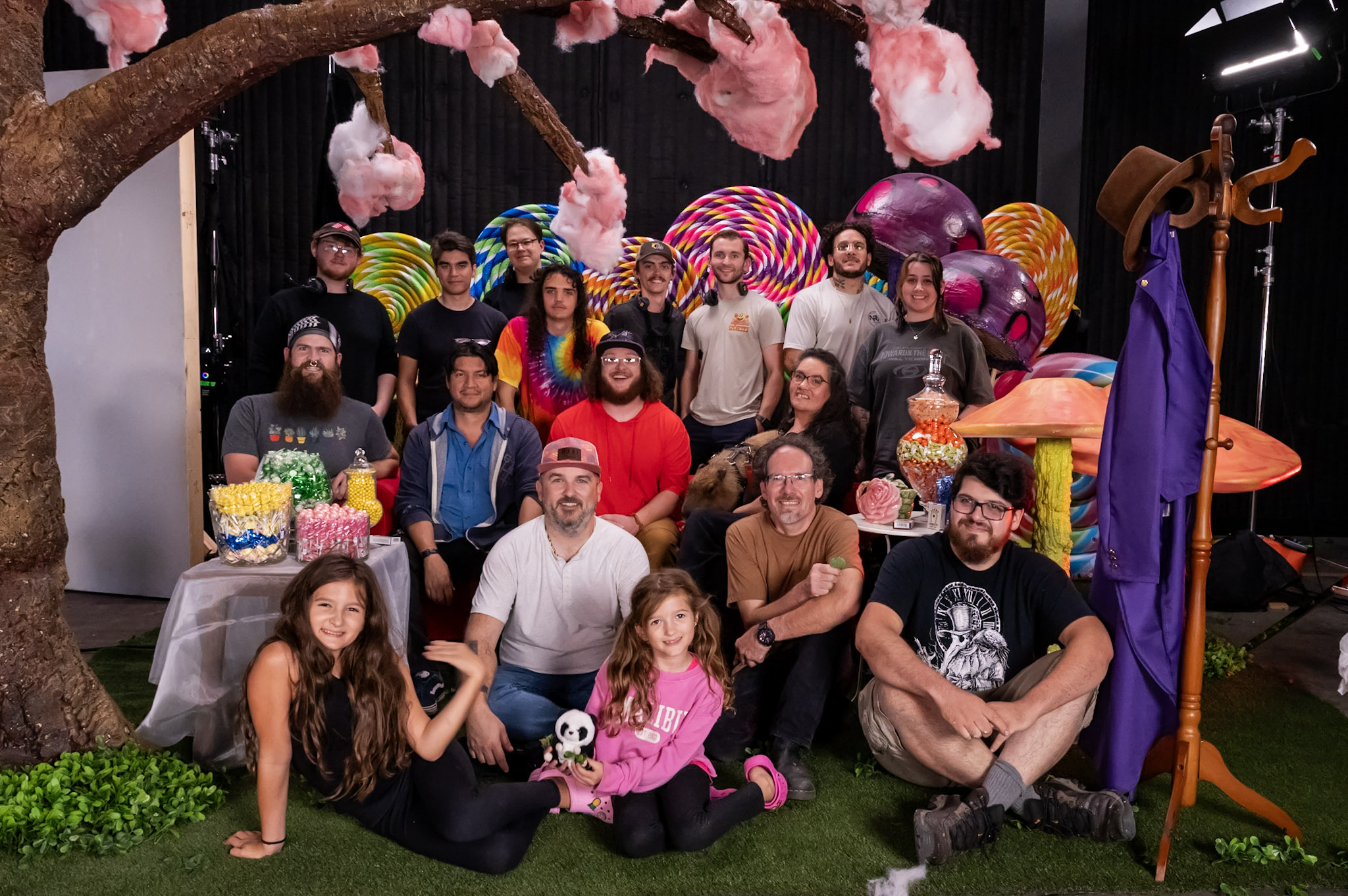 Group of people gathered around a table with colorful decorations and large candy props, some sitting and some standing.
