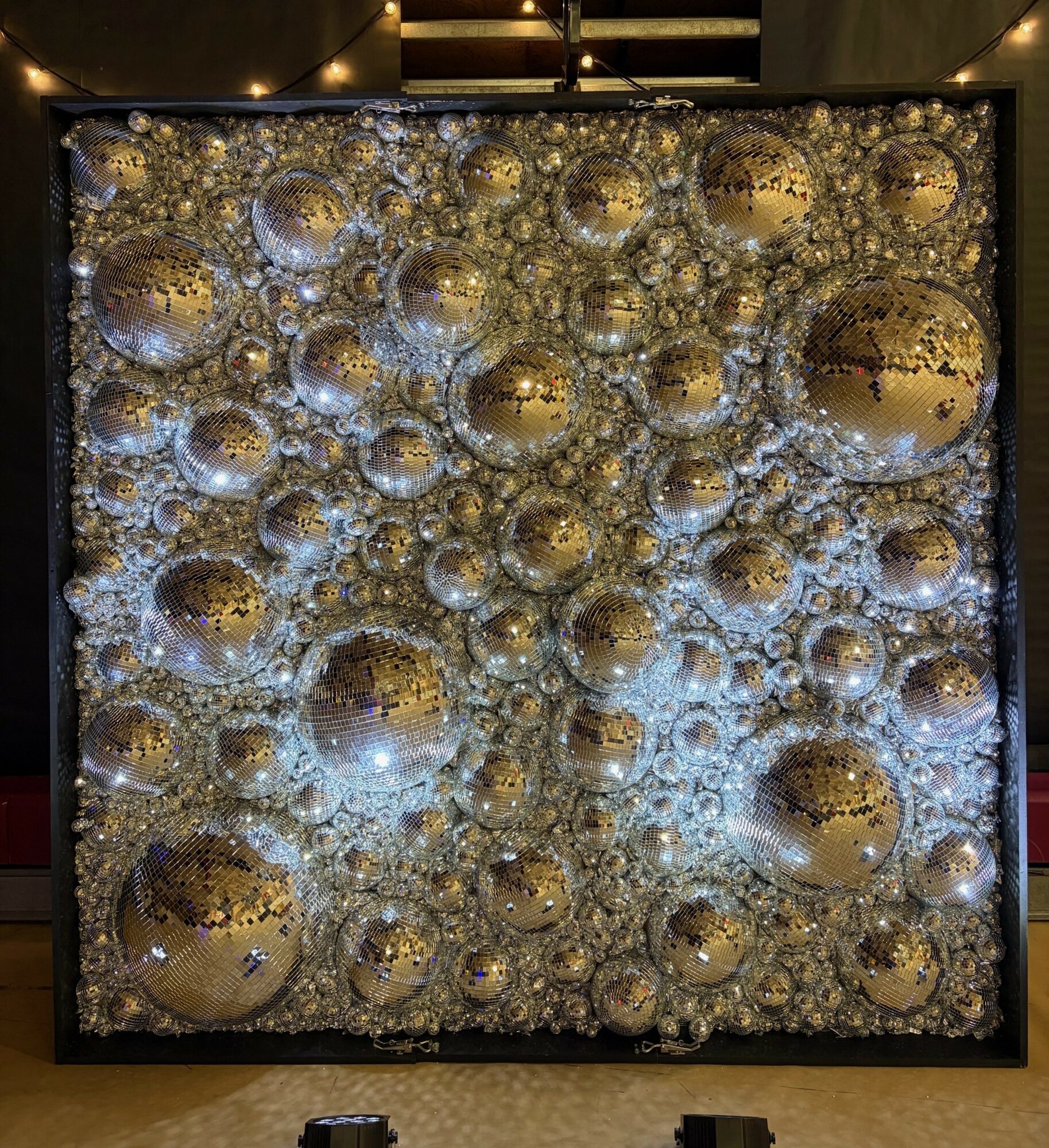 Decorative wall with numerous reflective silver and gold spherical ornaments and intricate patterns, illuminated by warm lighting.