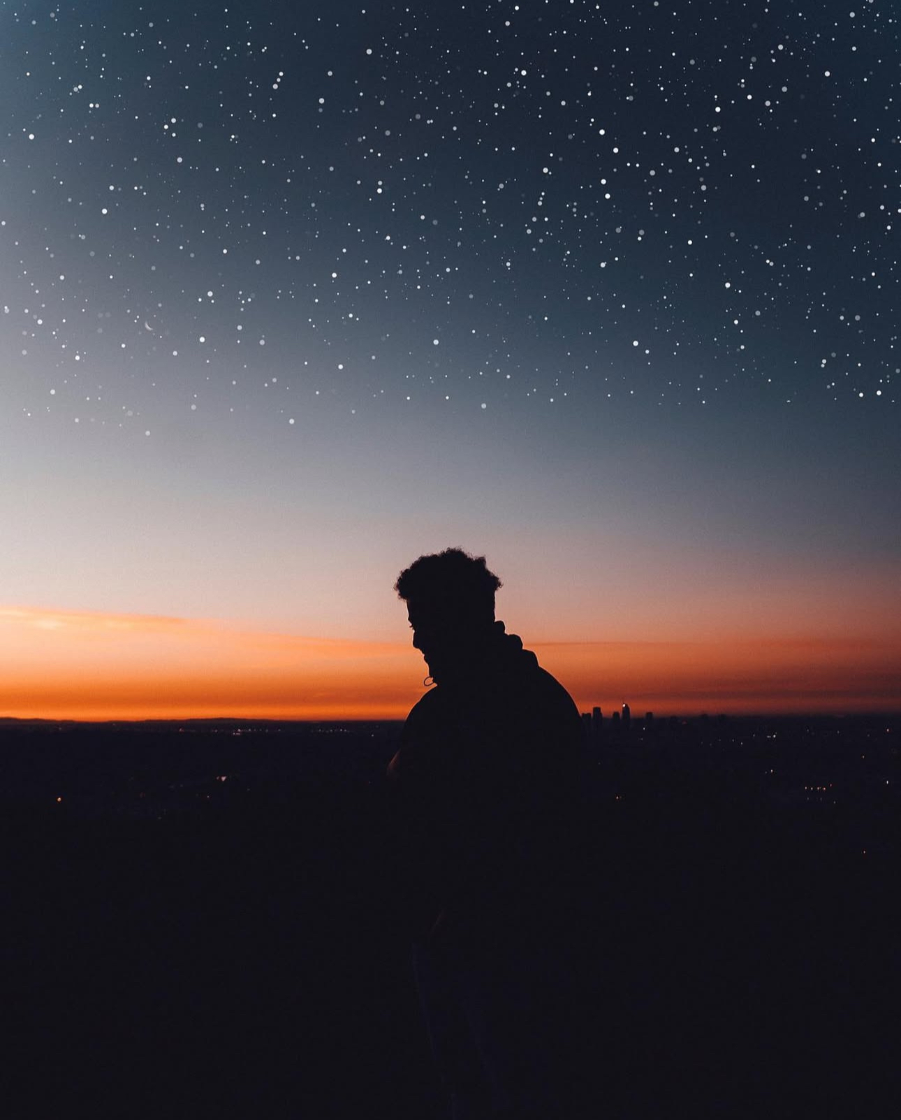 Silhouette of a person against a starry night sky with a sunset on the horizon.