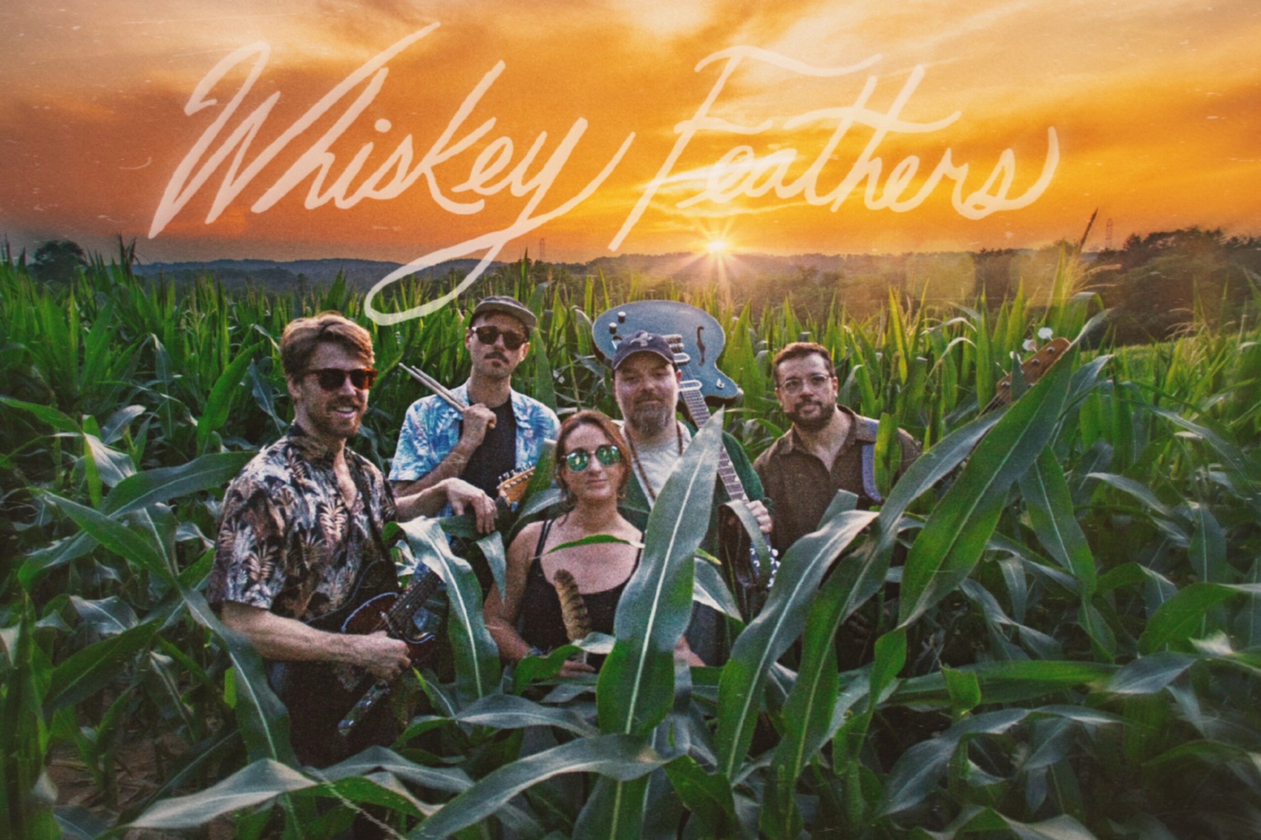 Group of five people standing in a cornfield at sunset, with a sunset sky in the background.