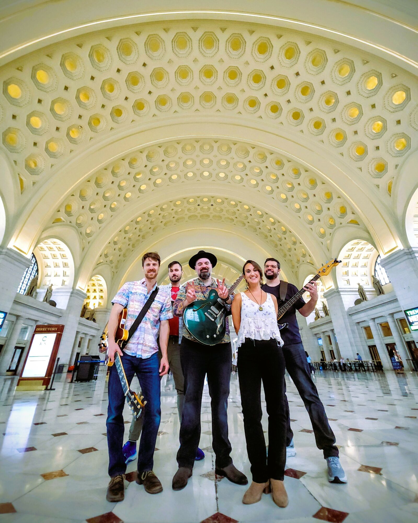 Group of five people standing inside a large, ornate building with a high, decorated ceiling and arches.