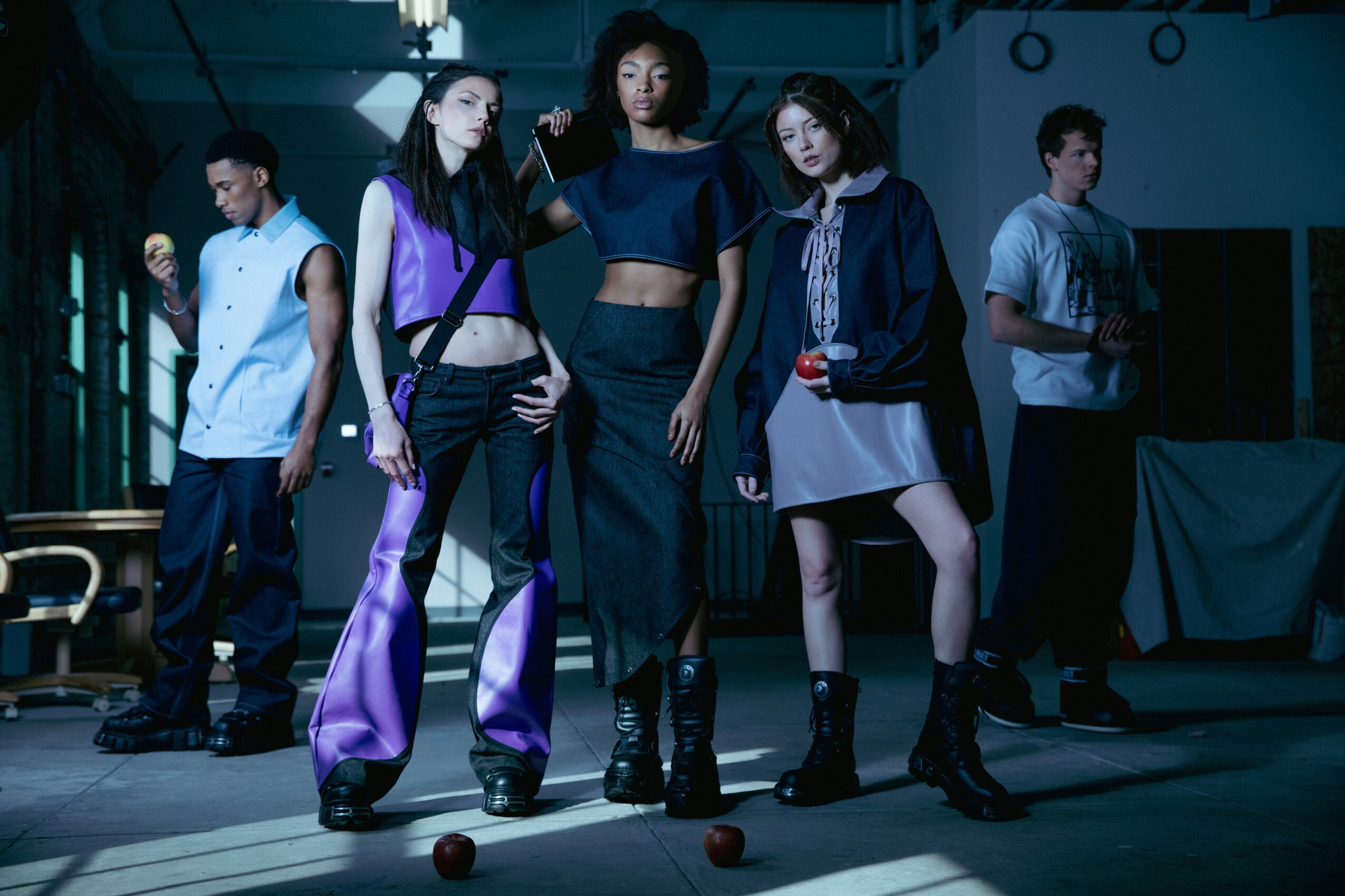 Group of five young people standing in a dimly lit indoor space, some looking at the camera, others looking away.