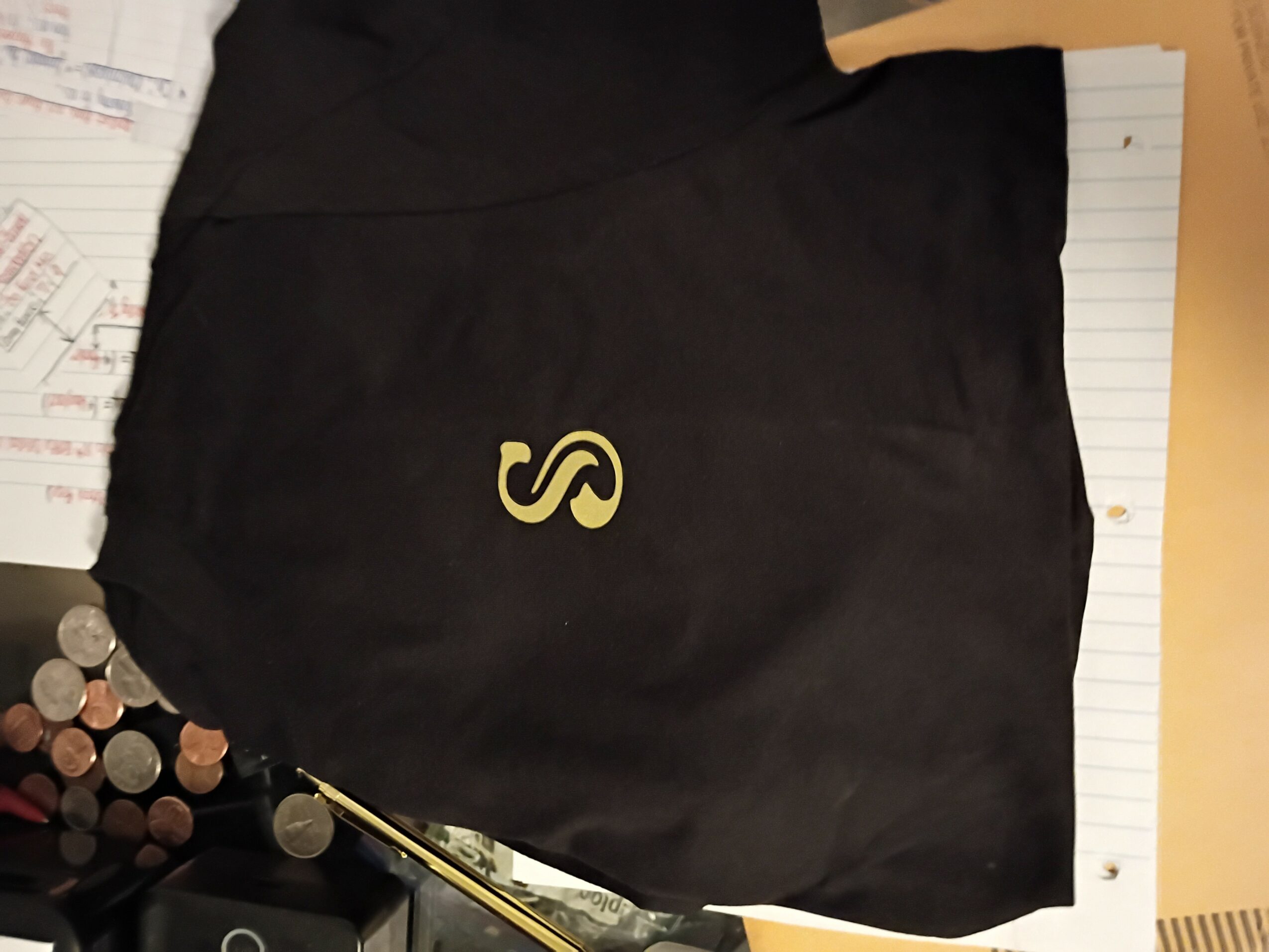 Black fabric with a yellow letter S, placed on a lined notepad, with coins and papers nearby.