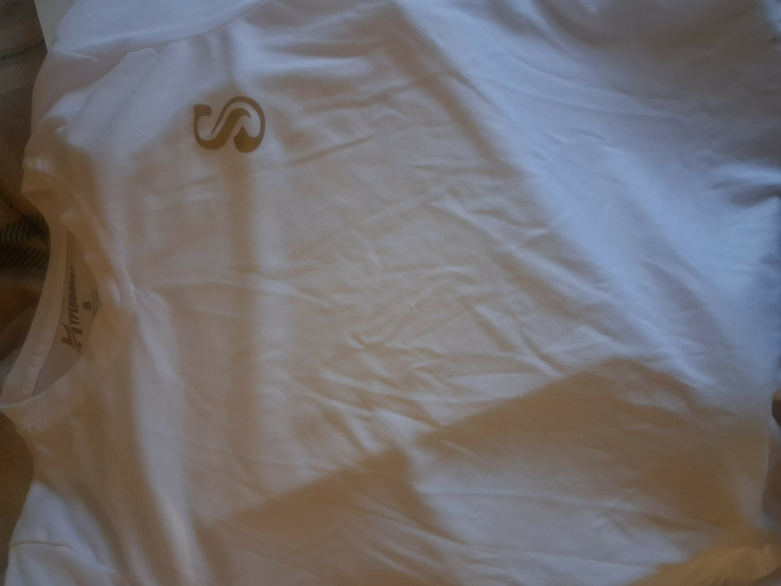 White fabric with a small gold logo near the top left corner, slightly wrinkled.