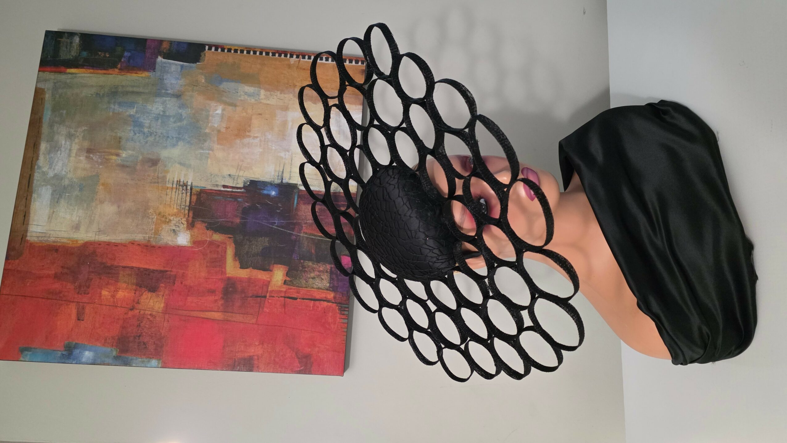 Hand holding a black, textured, oval-shaped object with a lattice-like structure, next to a colorful abstract painting.