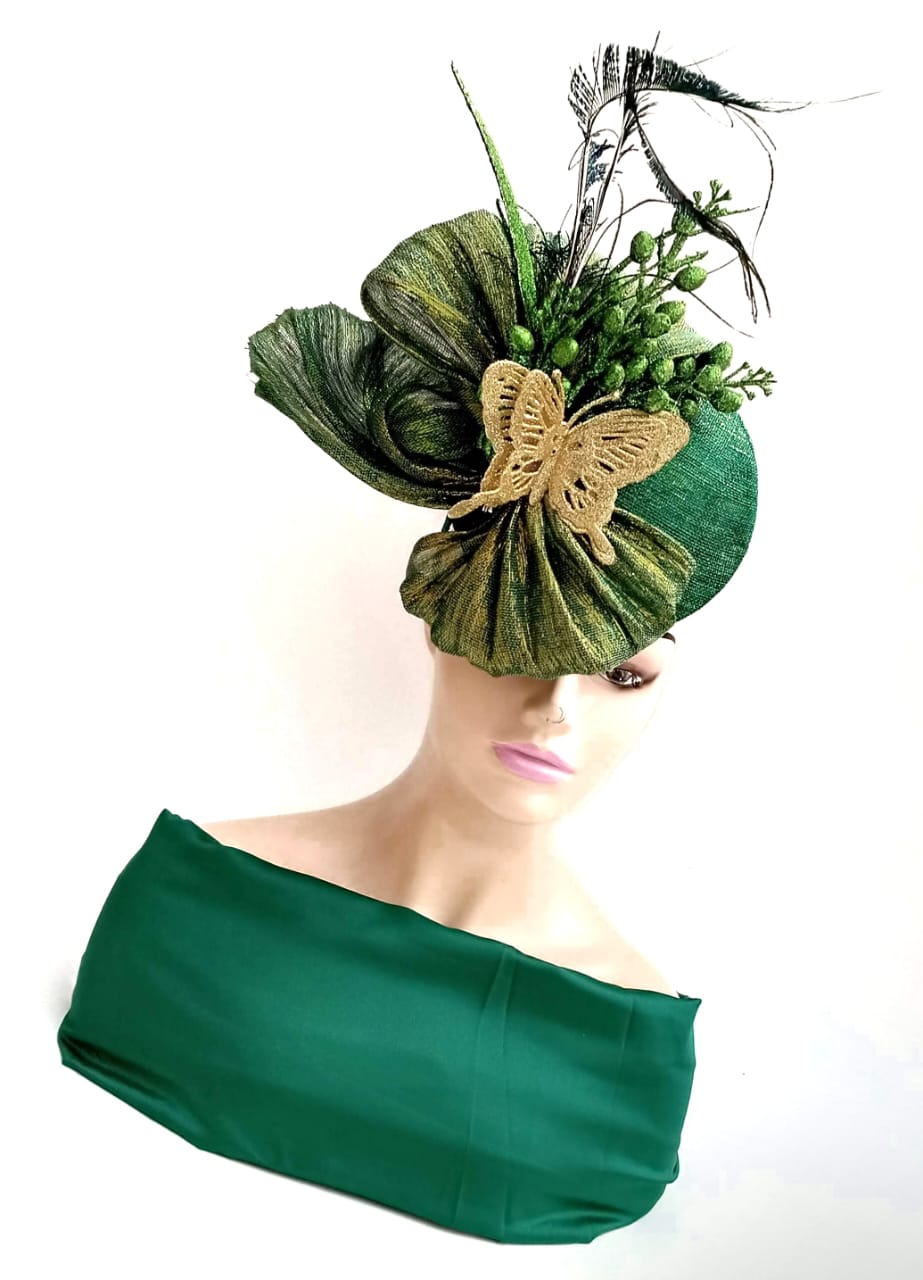 Person with a large green hat decorated with leaves, a butterfly, and flowers, wearing a green top, facing slightly downward.