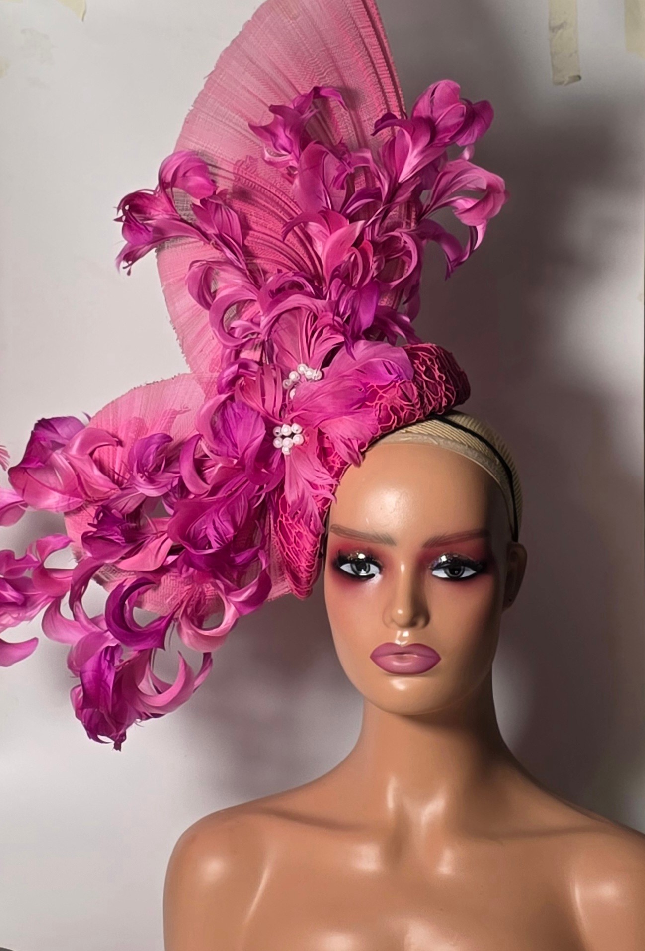 Person with elaborate pink feathered headpiece and makeup, facing forward, neutral background.