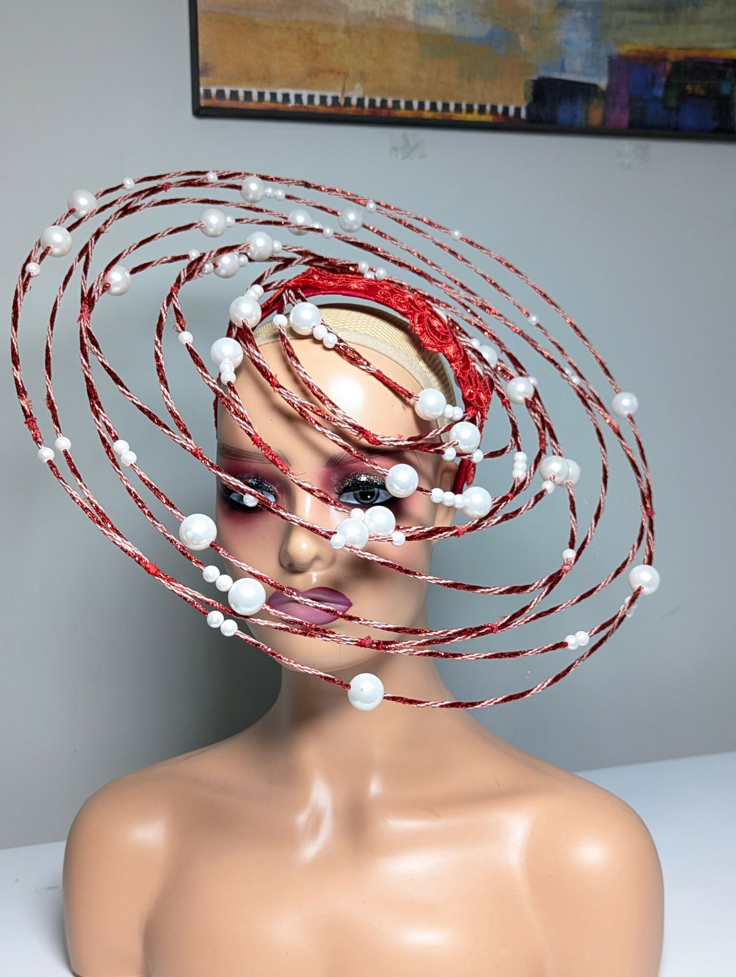 Person with an elaborate headpiece of red and white spirals and beads, covering face and head, indoors.